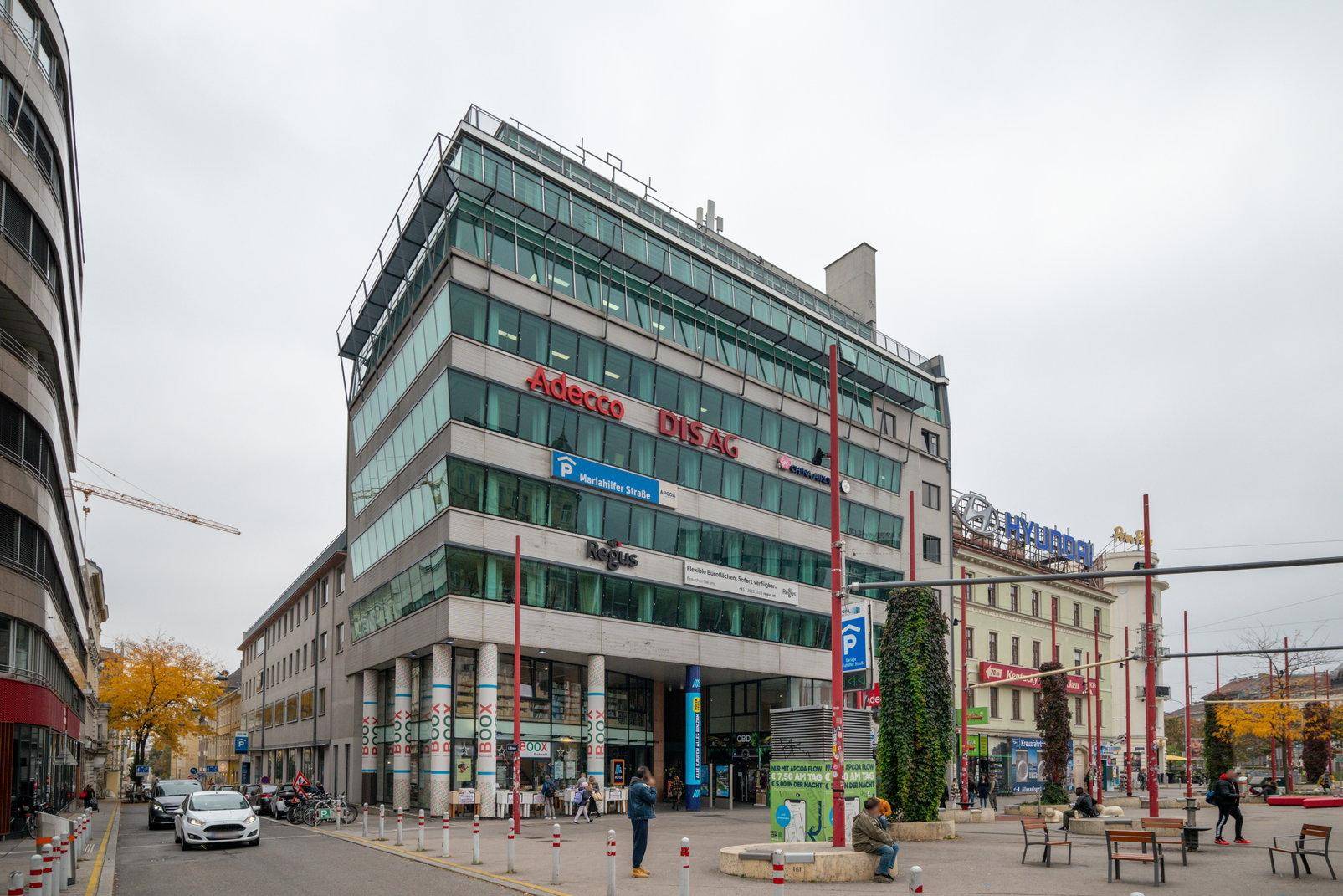 Modernes Geschäftsgebäude mit Glasfassade und mehreren Etagen an einer belebten Straße.