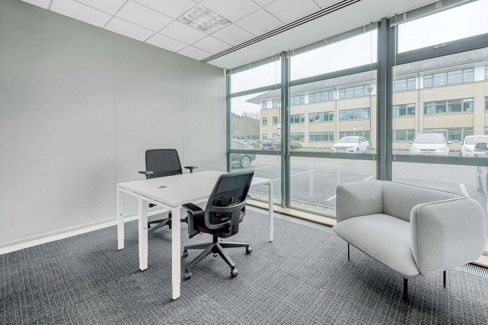 Helles Einzelbüro mit großen Fenstern, Teppichboden und minimalistischer Einrichtung, ideal für konzentriertes Arbeiten.