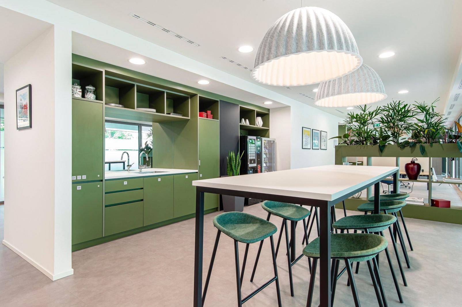 Moderne Teeküche mit grünen Schränken, Spüle und hoher Theke mit Barhockern, ideal für Pausen.