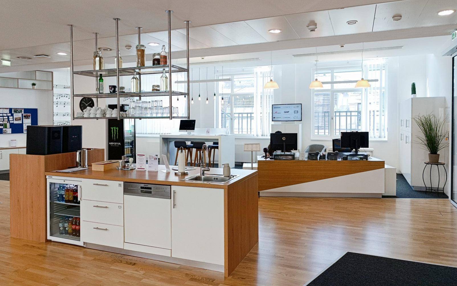Offener Bürobereich mit moderner Küchenzeile, Holzboden und Arbeitsplätzen im Hintergrund.