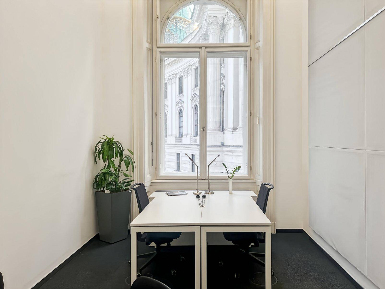 Kleines Büro mit hohem Bogenfenster, Blick auf ein historisches Gebäude und minimalistischer Einrichtung.