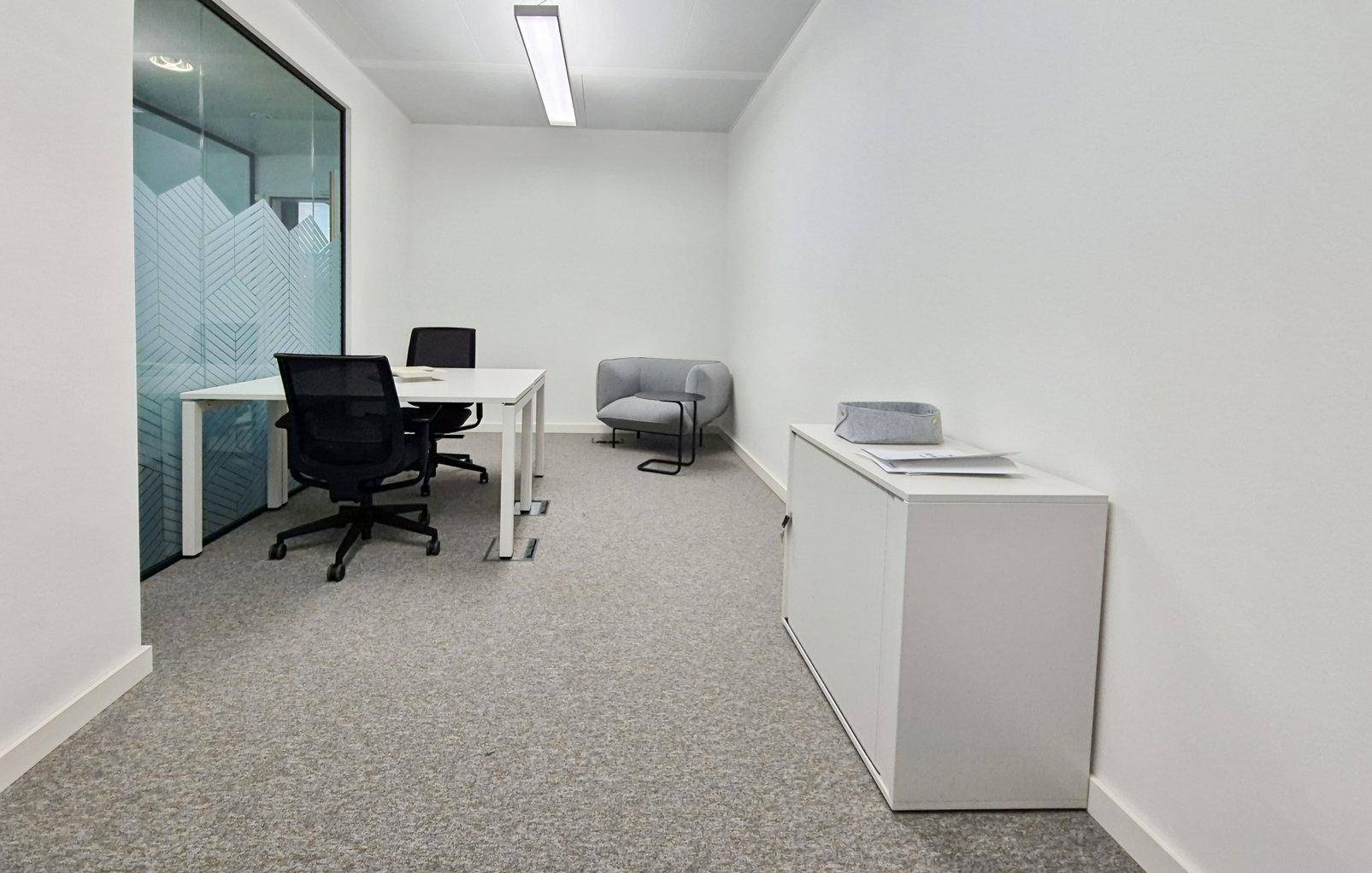 Kleines, modernes Büro mit Schreibtisch, Bürostuhl und einem Aktenschrank, getrennt durch eine Glaswand.