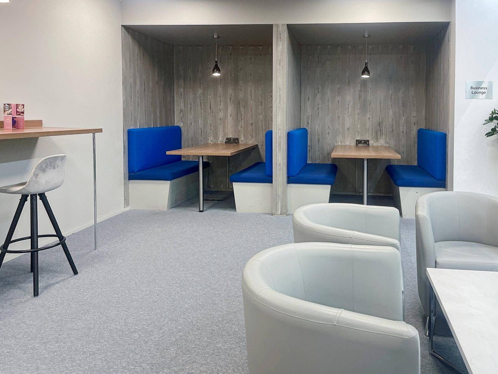 Gemütliche Business-Lounge mit blauen Sitzkabinen und modernen weißen Sesseln für entspannte Pausen oder informelle Treffen.