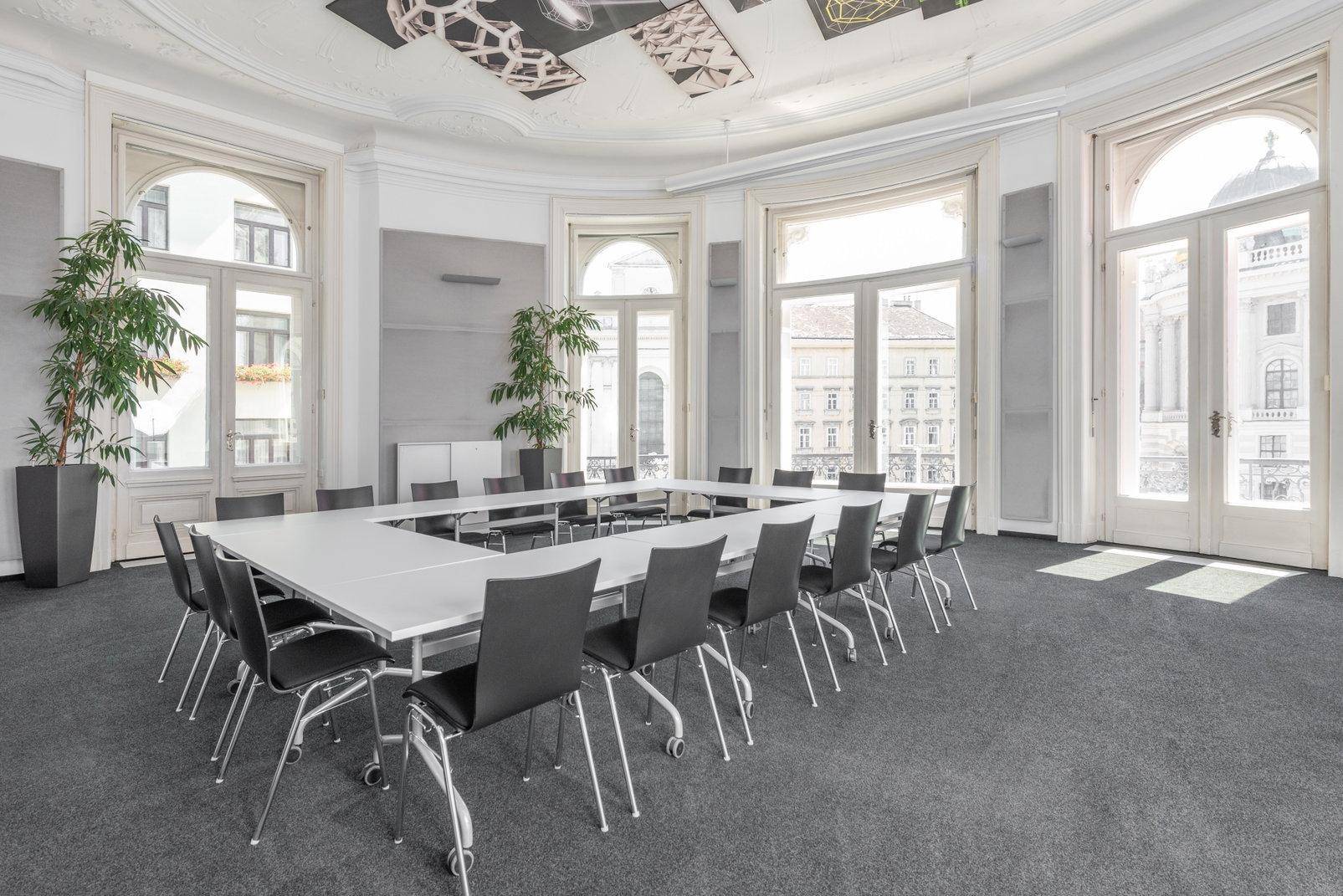 Großer Konferenzraum mit U-förmigem Tisch, hohen Decken, Stuckverzierungen und großen Bogenfenstern.