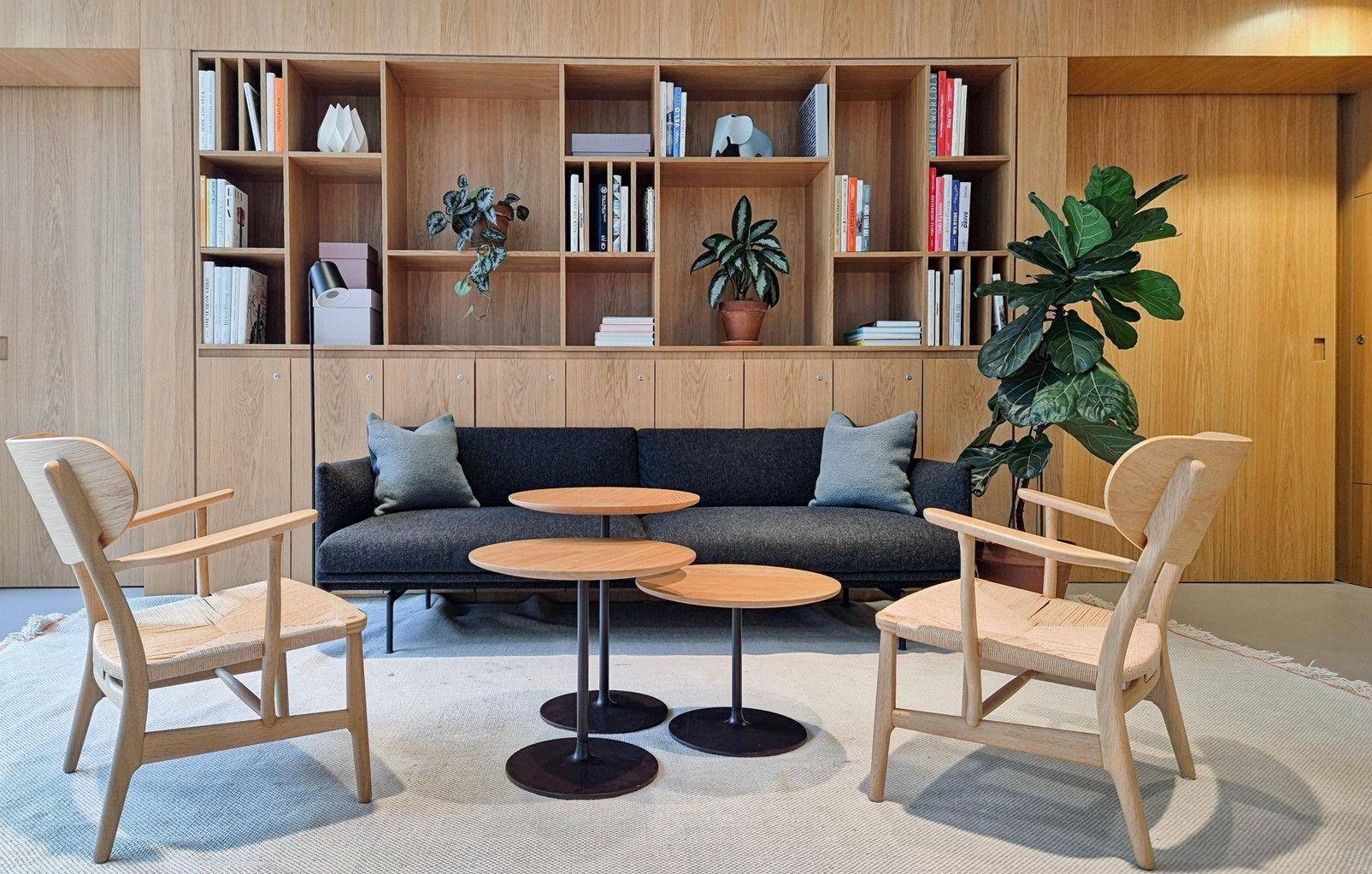 Gemütlicher Loungebereich mit Sofa, Sesseln und einer Holzwand mit integrierten Regalen und Pflanzen.
