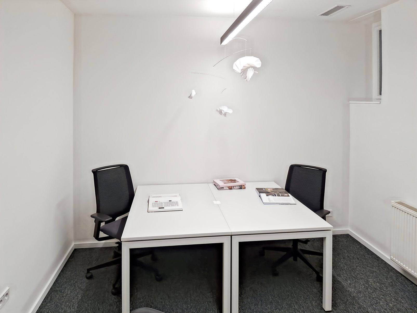 Kleines, helles Büro mit zwei Arbeitsplätzen, minimalistischer Dekoration und Teppichboden.