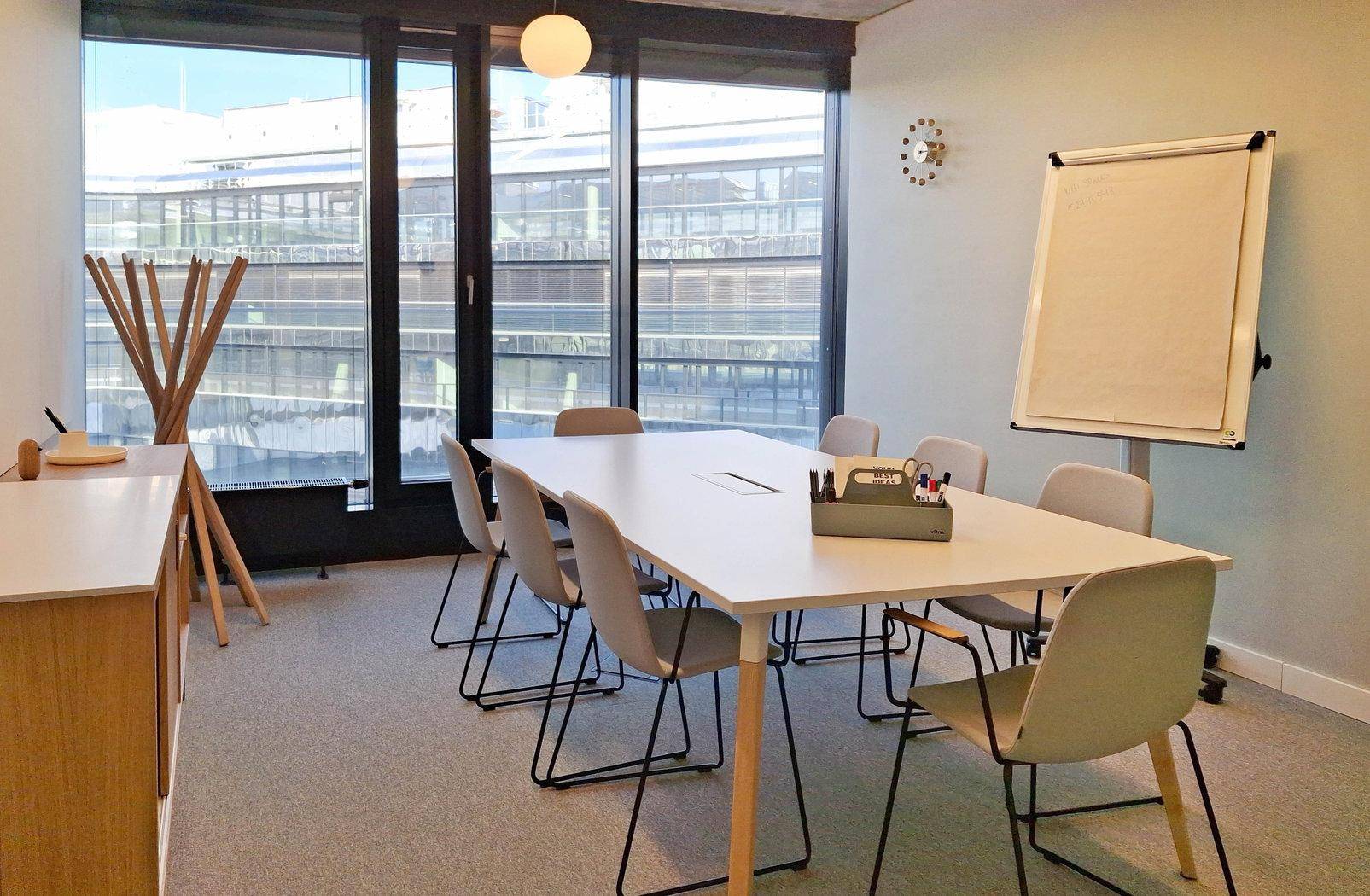 Heller Besprechungsraum mit großem Tisch, Whiteboard und viel Tageslicht durch bodentiefe Fenster.