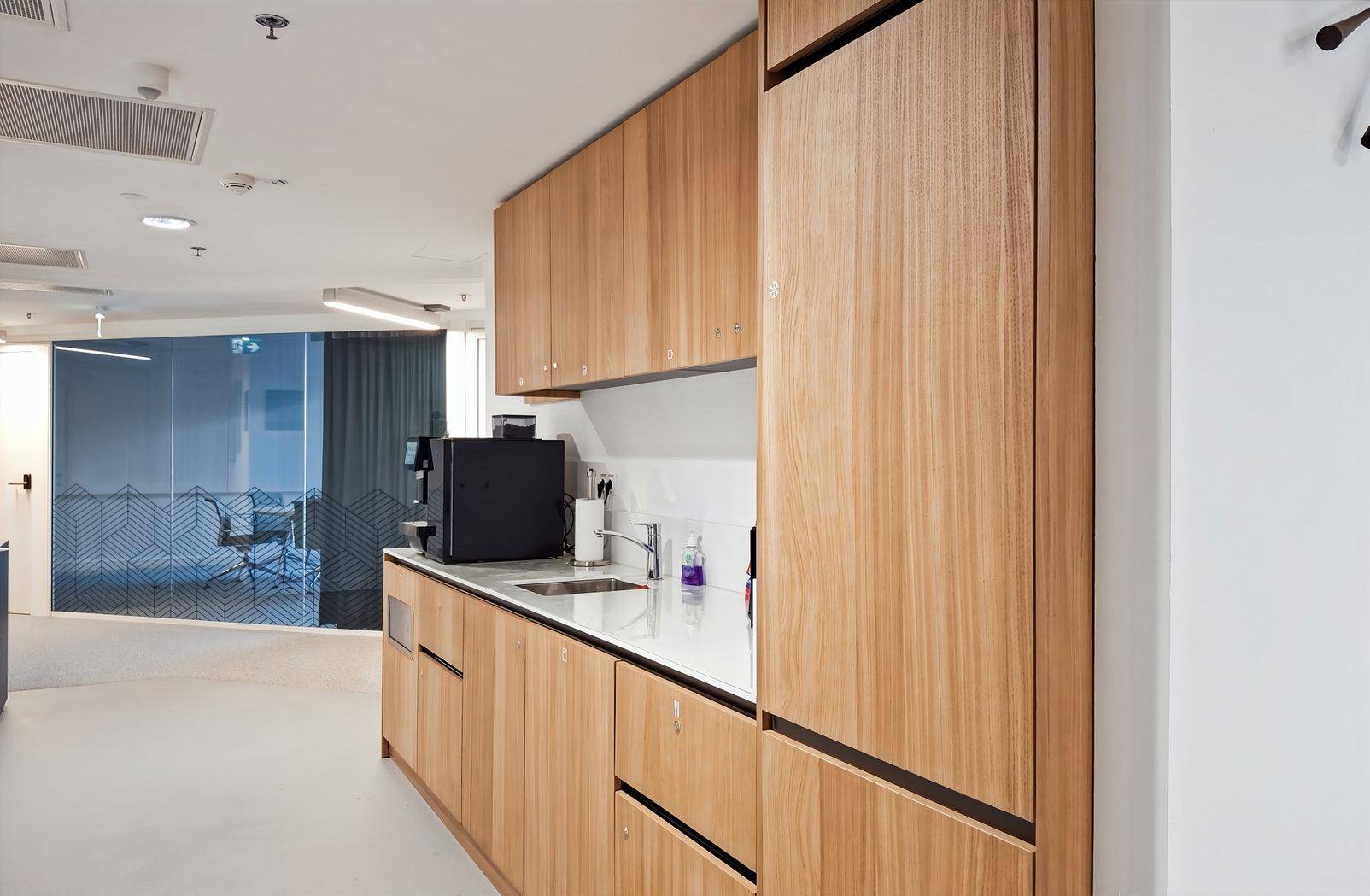 Moderne Teeküche mit Holzschränken, weißer Arbeitsplatte und integrierten Geräten für Mitarbeiter.