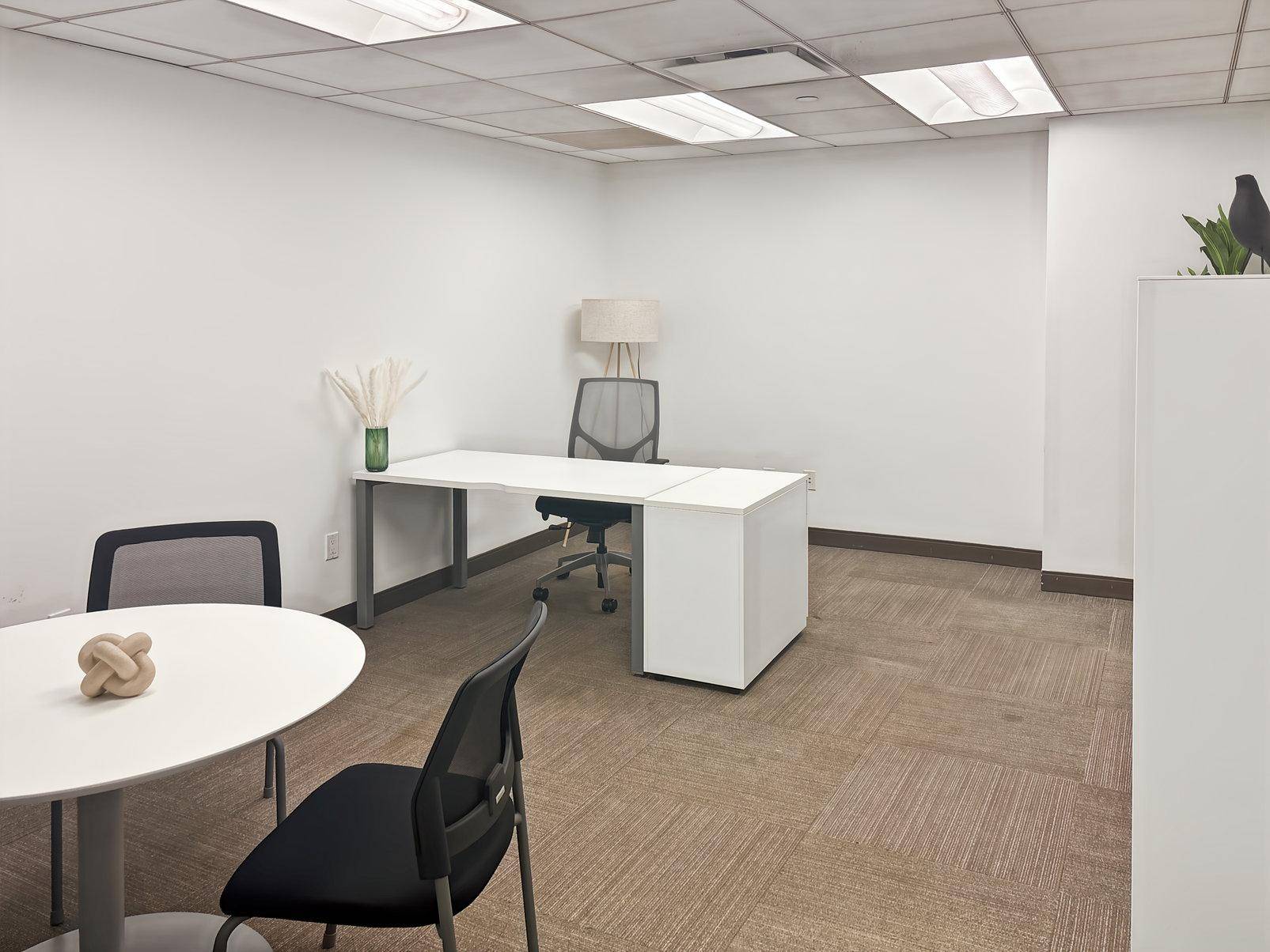 Geräumiges Einzelbüro mit einem großen Schreibtisch, beigem Teppichboden und einer kleinen Sitzecke.
