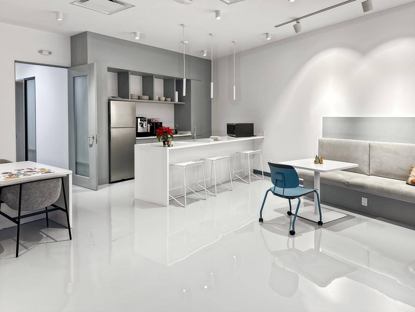 Helle, moderne Büroküche mit weißer Theke, Barhockern, Kühlschrank und integriertem Sitzbereich für Pausen.