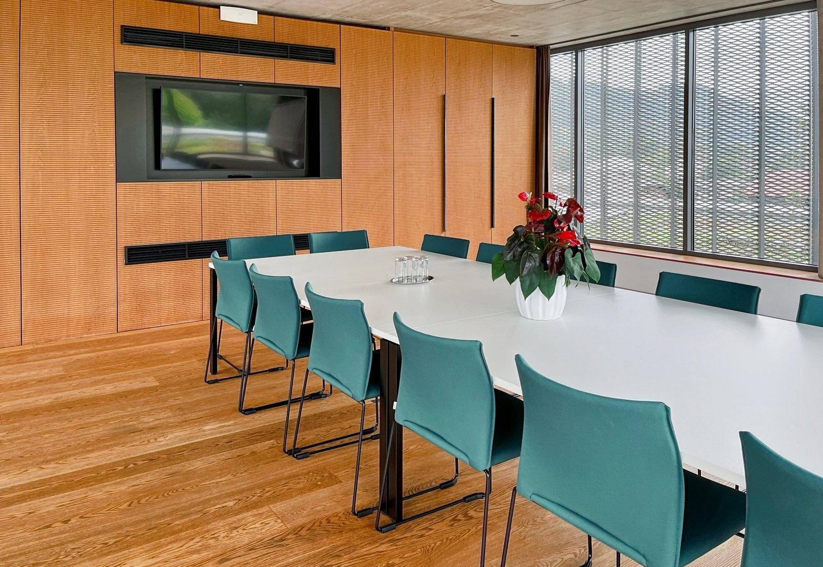 Moderner Konferenzraum mit großem Tisch, eleganter Holzverkleidung und integriertem Bildschirm.