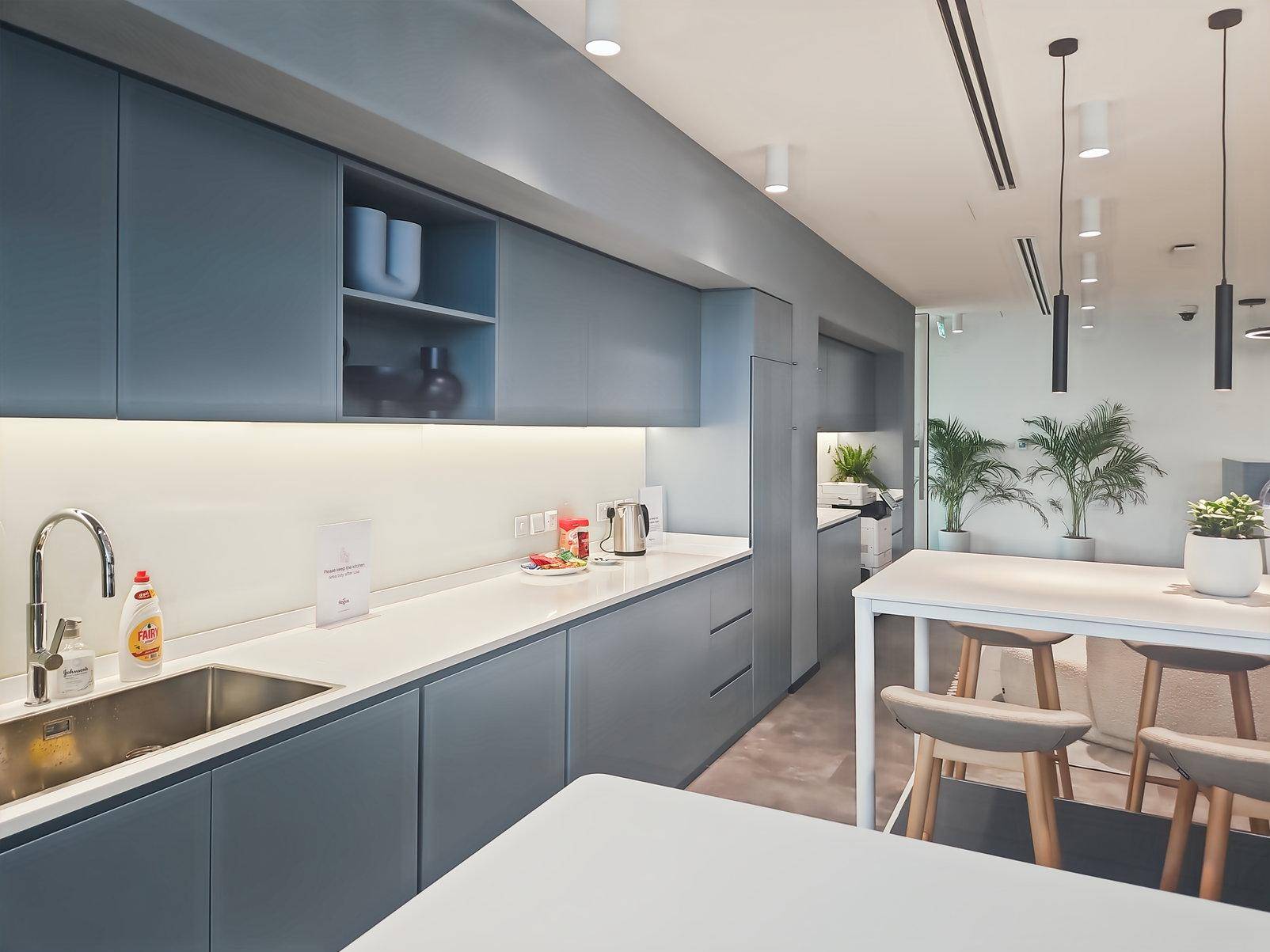Moderne Büroküche mit blauen Schränken, weißer Arbeitsplatte und integrierter Spüle.