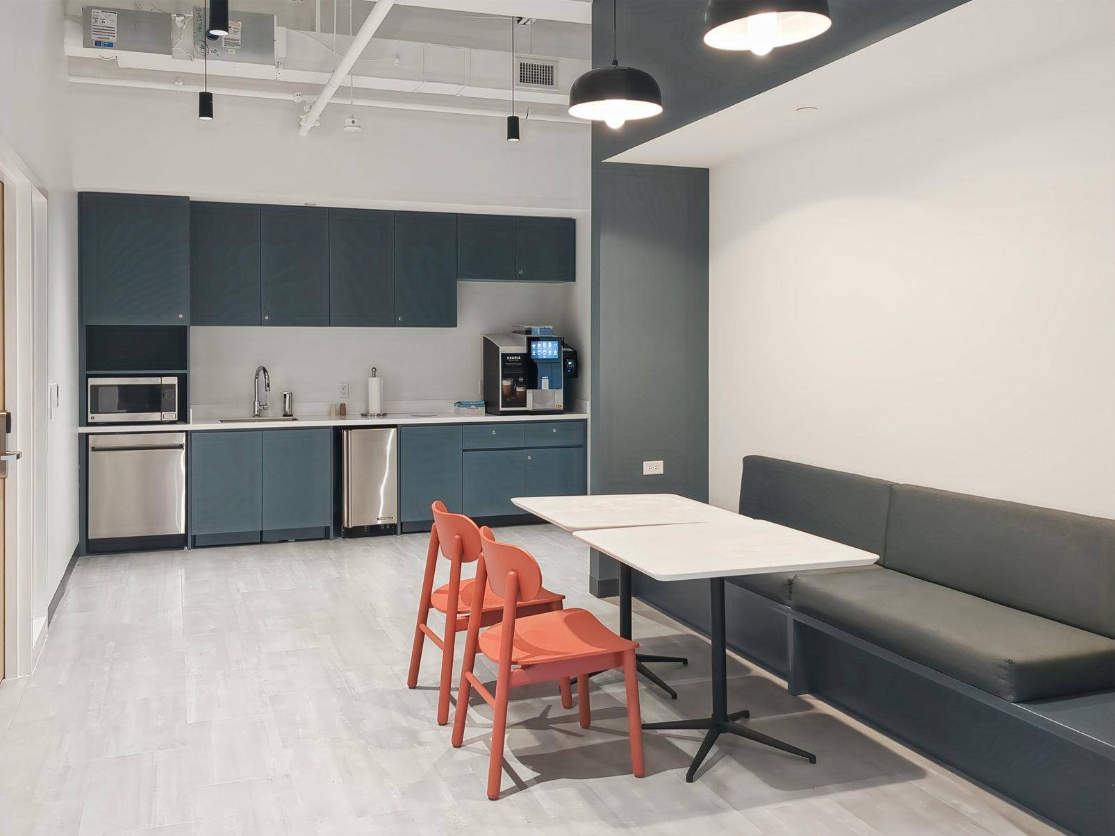 Moderne Teeküche mit blauen Schränken, integrierten Geräten und einem Sitzbereich mit Bank.