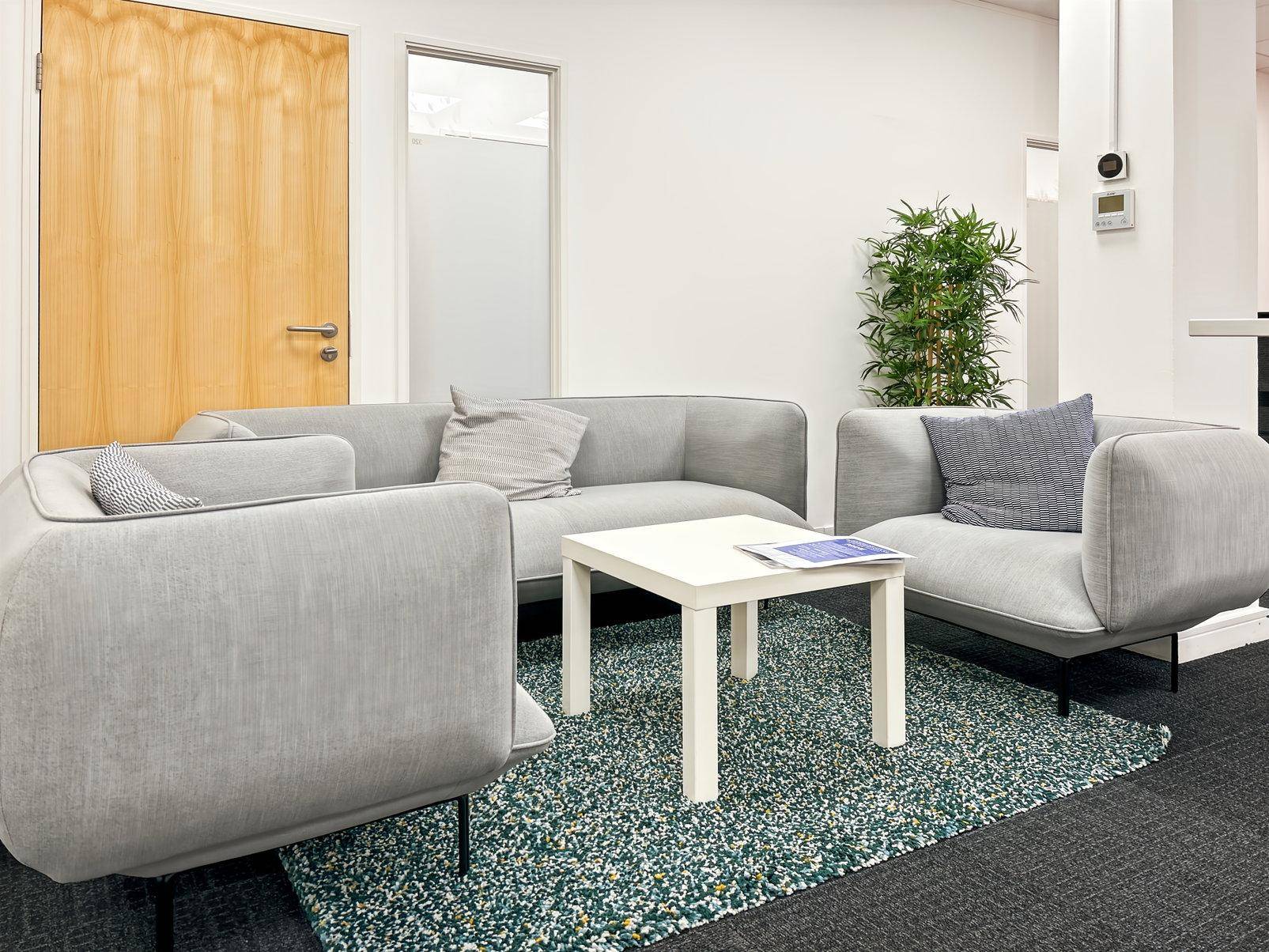 Gemütlicher Loungebereich mit bequemen grauen Sofas, einem weißen Couchtisch und einem farbigen Teppich.