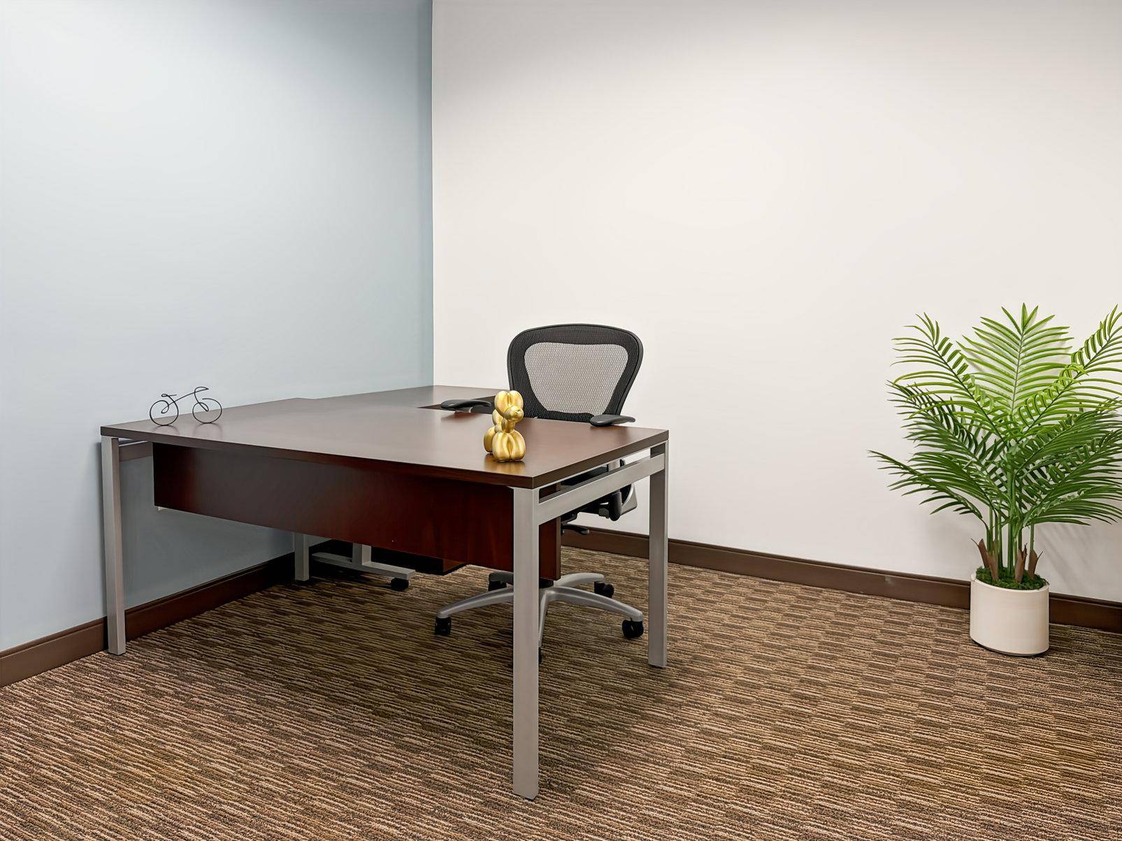 Helles Büro mit einem Schreibtisch, Bürostuhl, einer Pflanze und einem Teppichboden in Brauntönen.