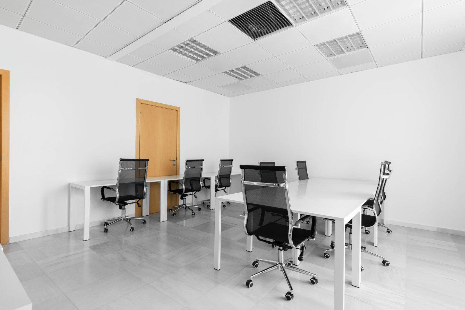 Helles Büro mit mehreren Schreibtischen, Bürostühlen und einem hellen Fliesenboden.