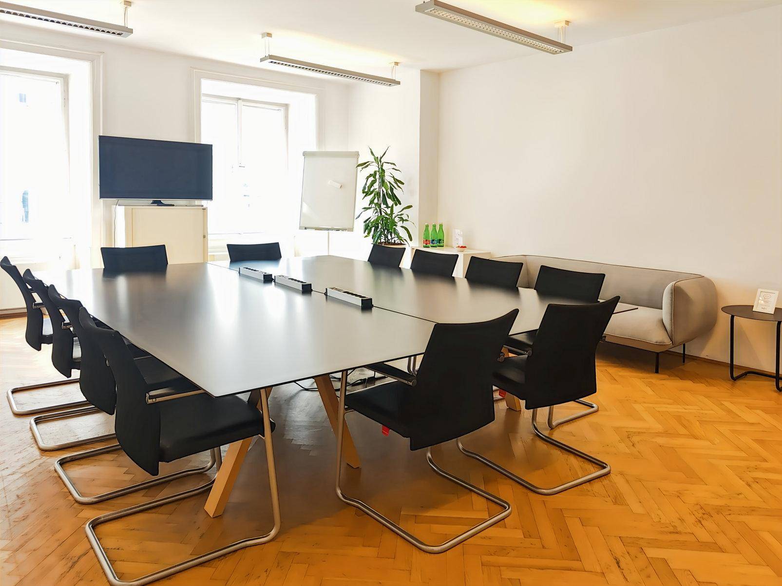 Eleganter Konferenzraum mit großem schwarzen Tisch, bequemen Stühlen und einem Sofa.