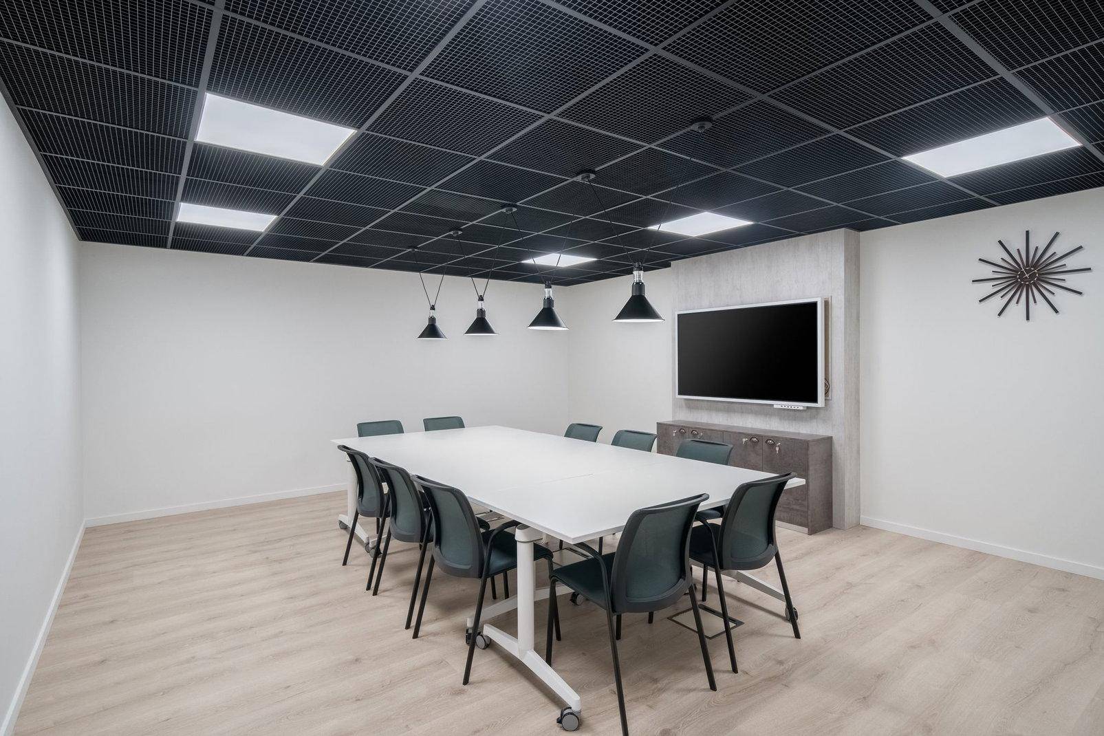 Moderner Konferenzraum mit großem Tisch, schwarzen Stühlen, Holzfußboden und abgehängter Decke.
