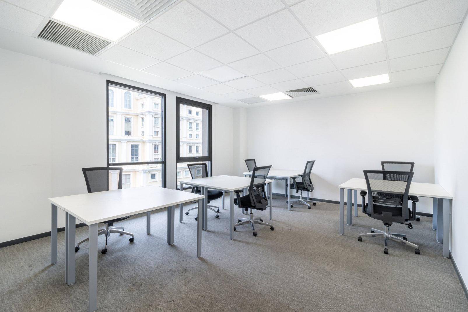 Helles Büro mit mehreren Arbeitsplätzen, großen Fenstern und Teppichboden.