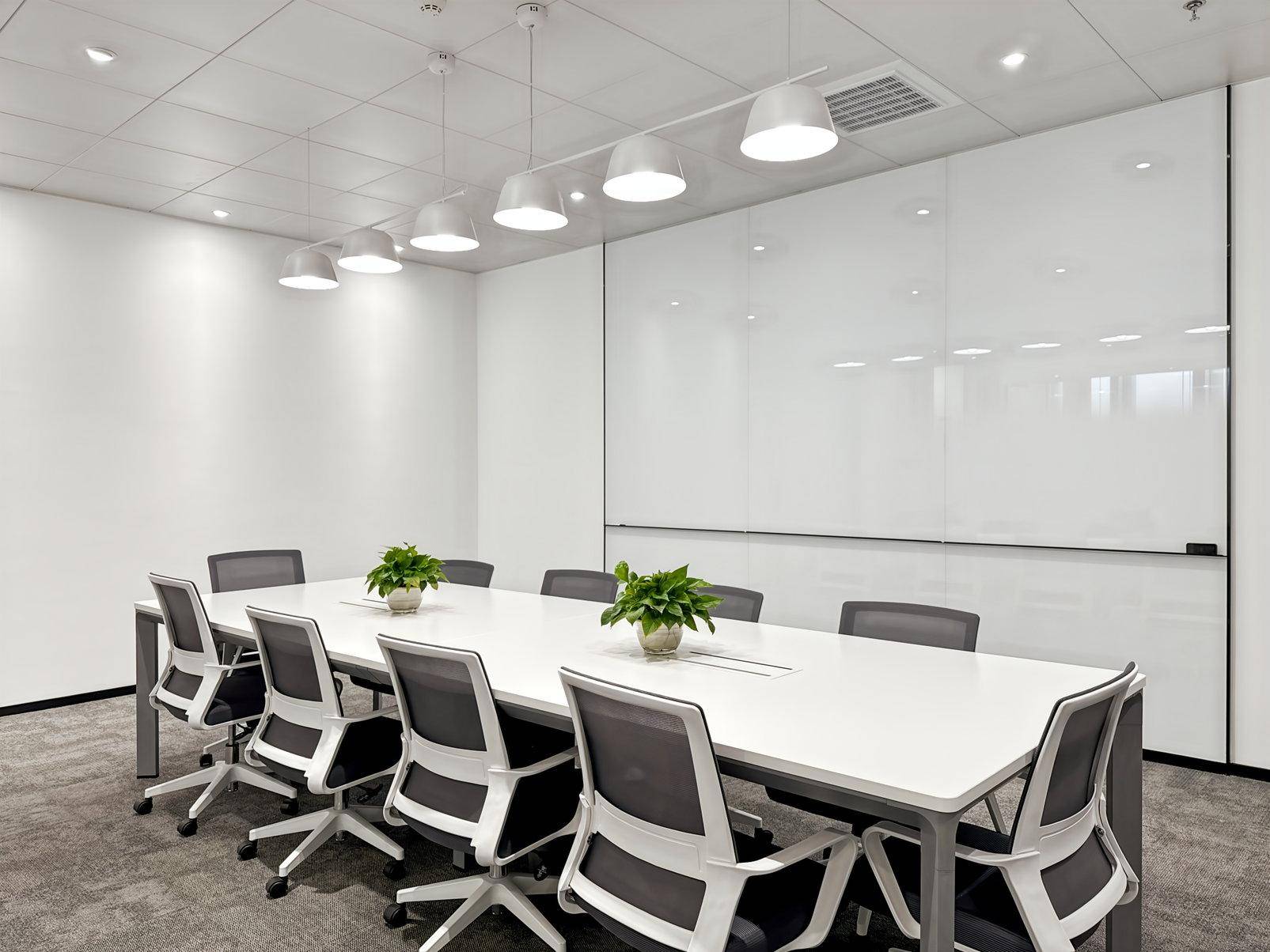 Heller Konferenzraum mit langem weißen Tisch, modernen Stühlen und großer Whiteboard-Wand.