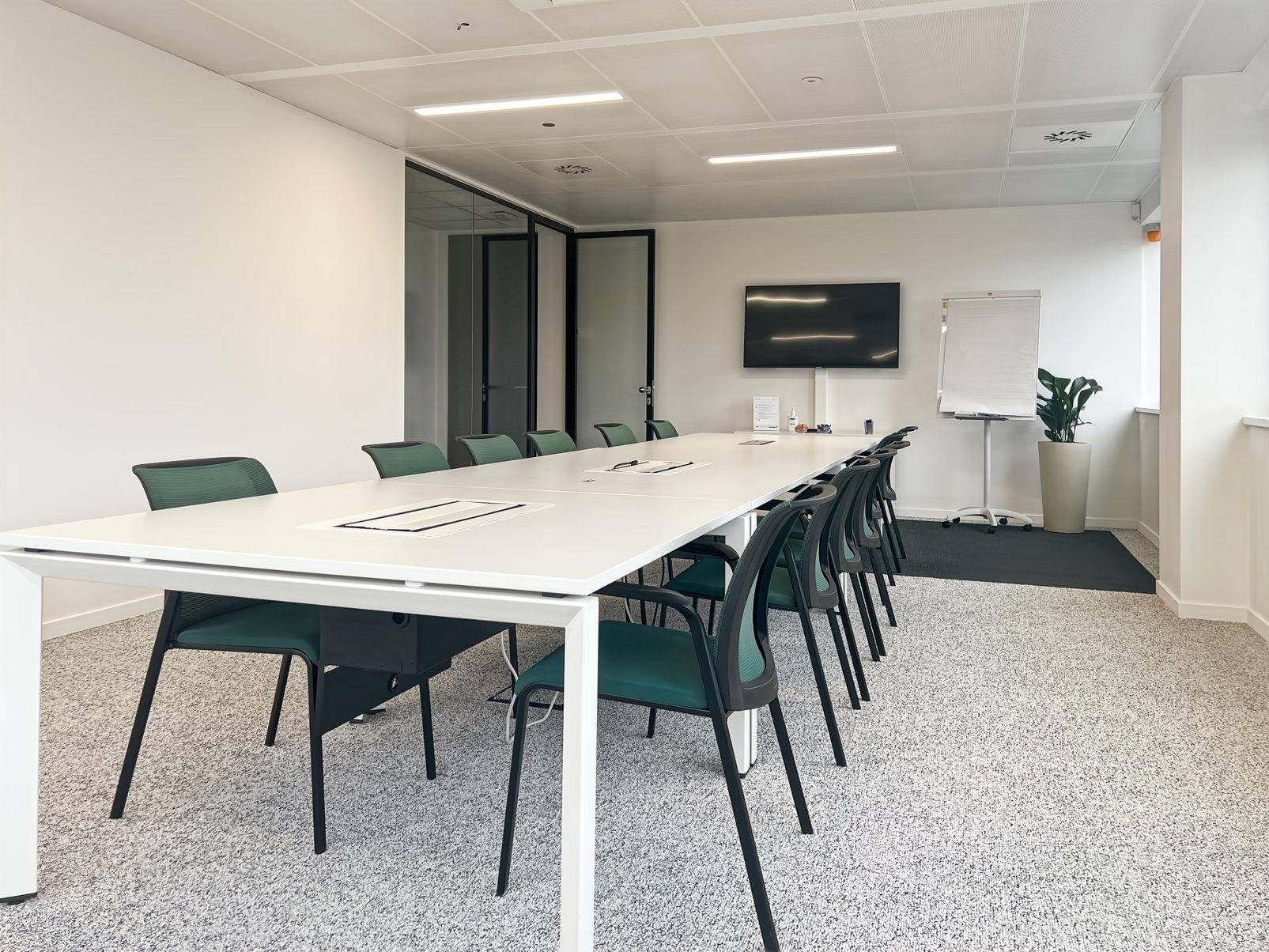 Heller Konferenzraum mit großem Tisch, bequemen Stühlen, Wandfernseher und einem Whiteboard.