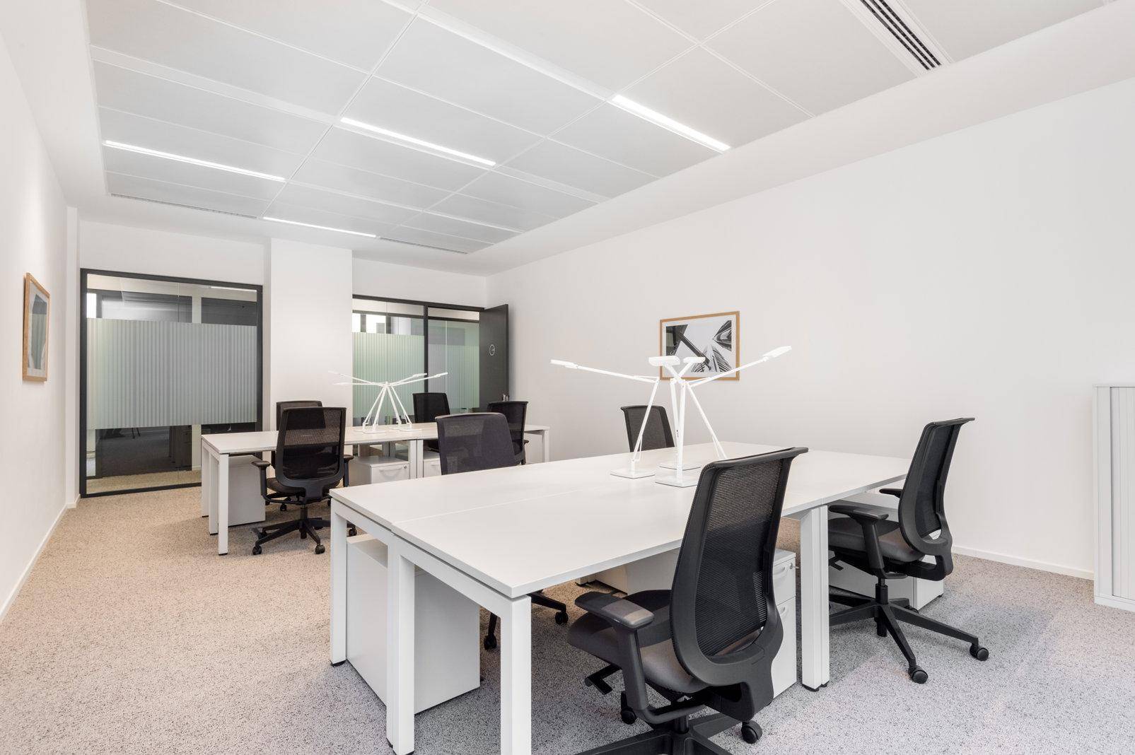 Heller Großraumbüro mit mehreren Arbeitsplätzen, modernen Schreibtischen und ergonomischen Bürostühlen.