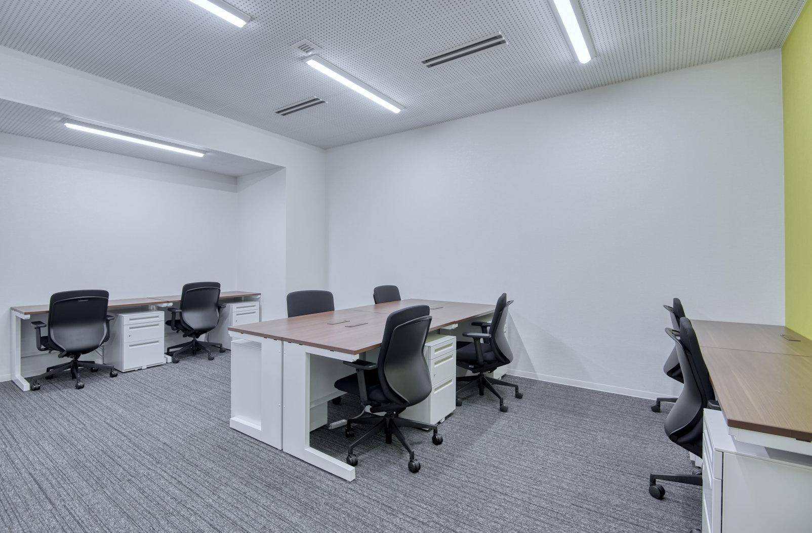 Geräumiger Büroraum mit mehreren Schreibtischen, ergonomischen Stühlen und Teppichboden.