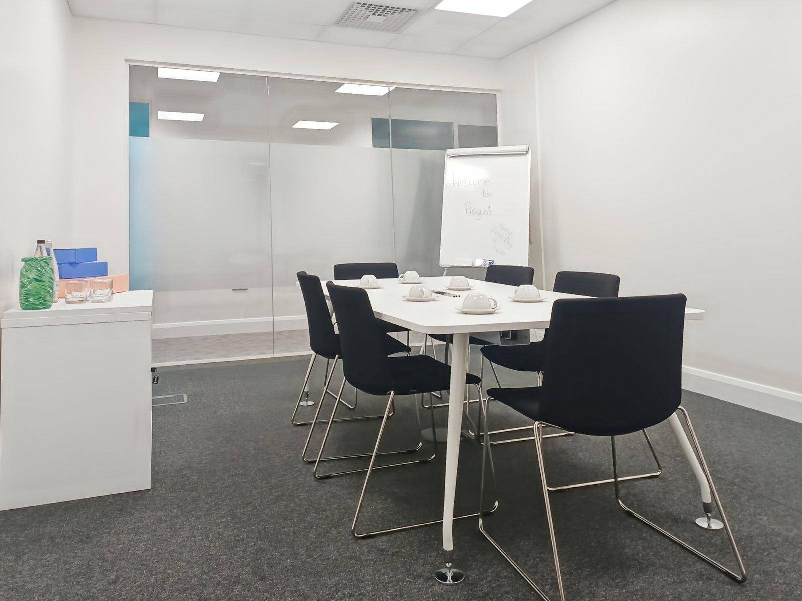 Heller Konferenzraum mit großem Tisch, schwarzen Stühlen, Whiteboard und Glaswand für Besprechungen.