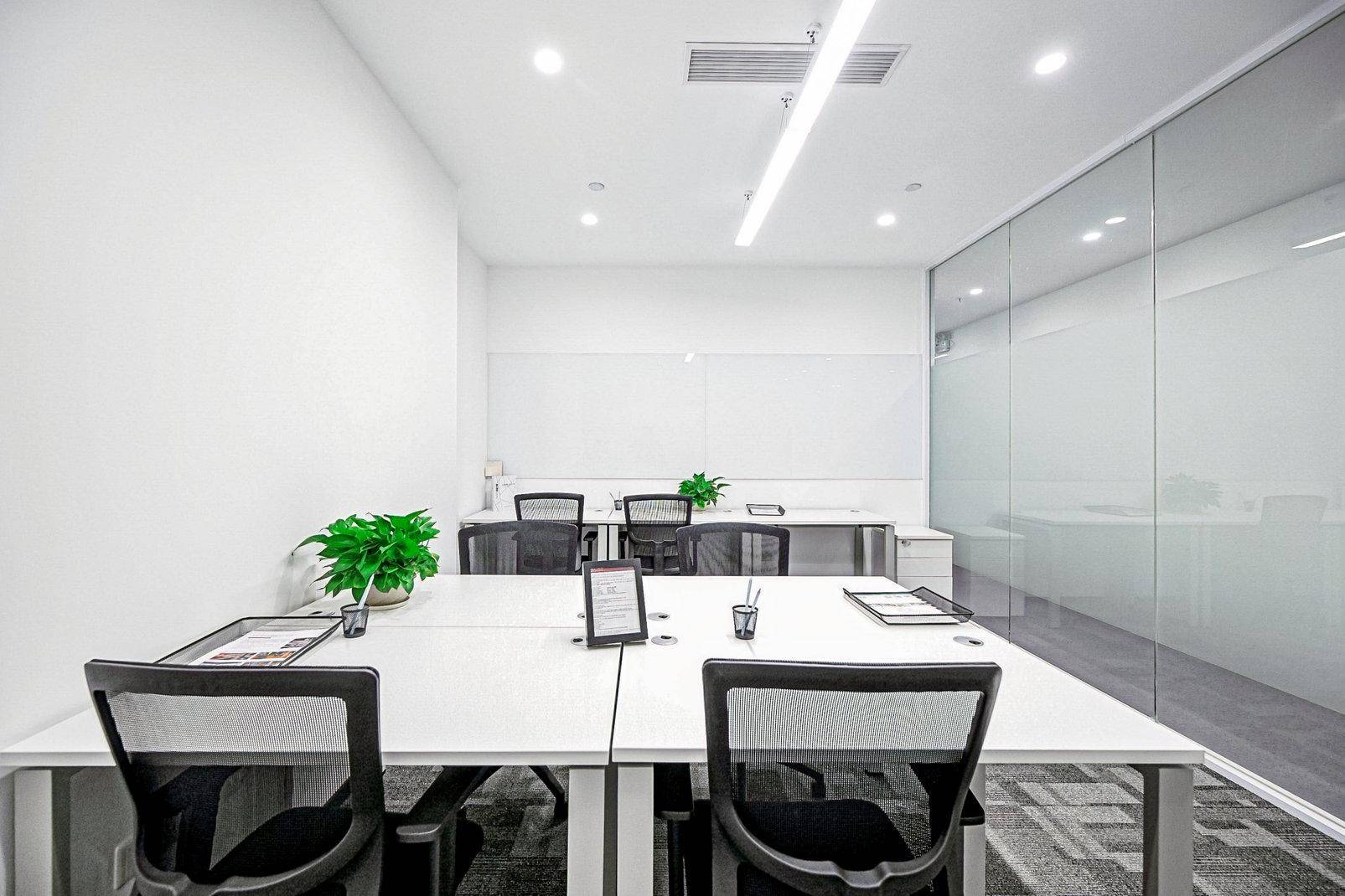 Helles und modernes Büro mit mehreren Arbeitsplätzen, Glaswand und minimalistischer Einrichtung.