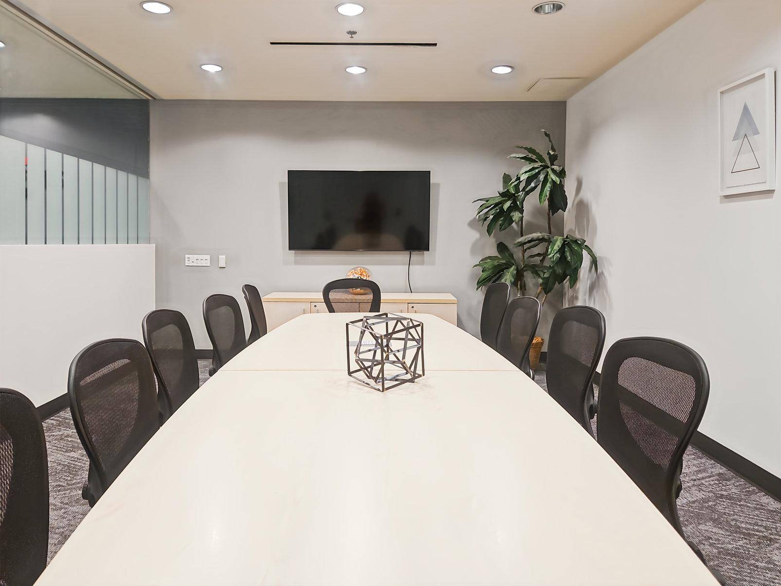 Geräumiger Konferenzraum mit langem Tisch, ergonomischen Stühlen und einem großen Wandbildschirm.
