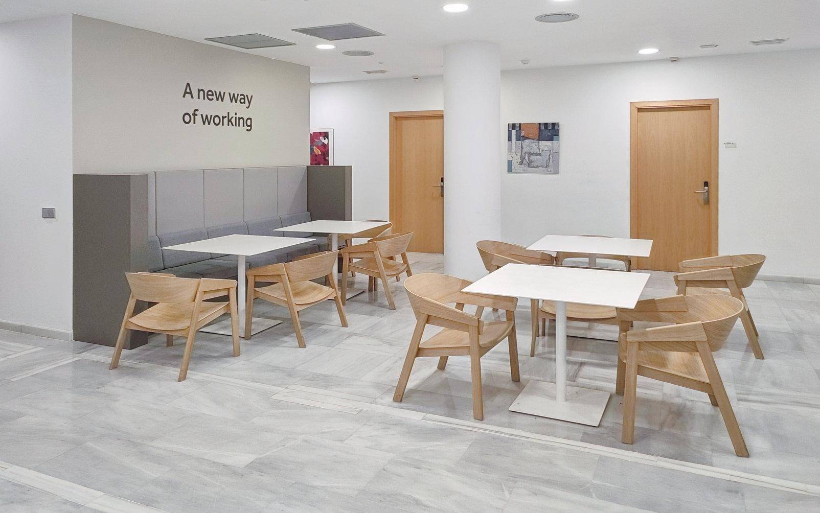Heller Loungebereich mit Holztischen, modernen Holzstühlen und einer Sitzbank.