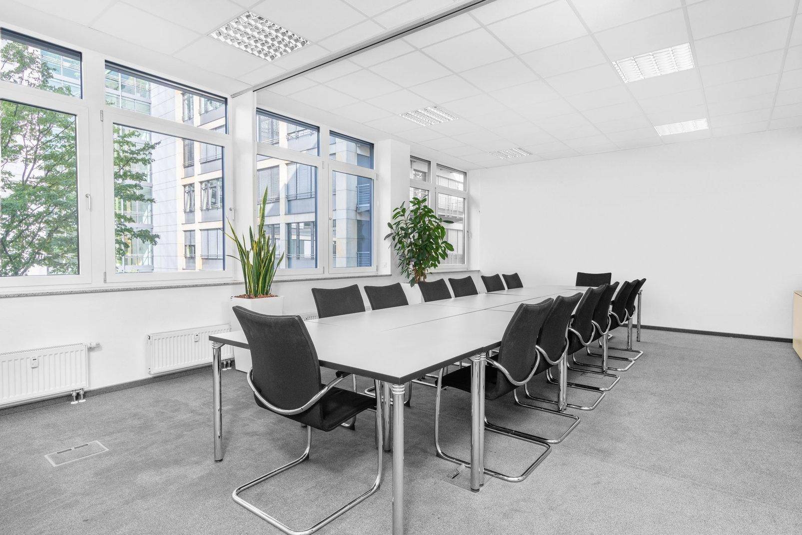 Geräumiger Konferenzraum mit langem Tisch, schwarzen Stühlen und großen Fenstern, die viel Tageslicht hereinlassen.