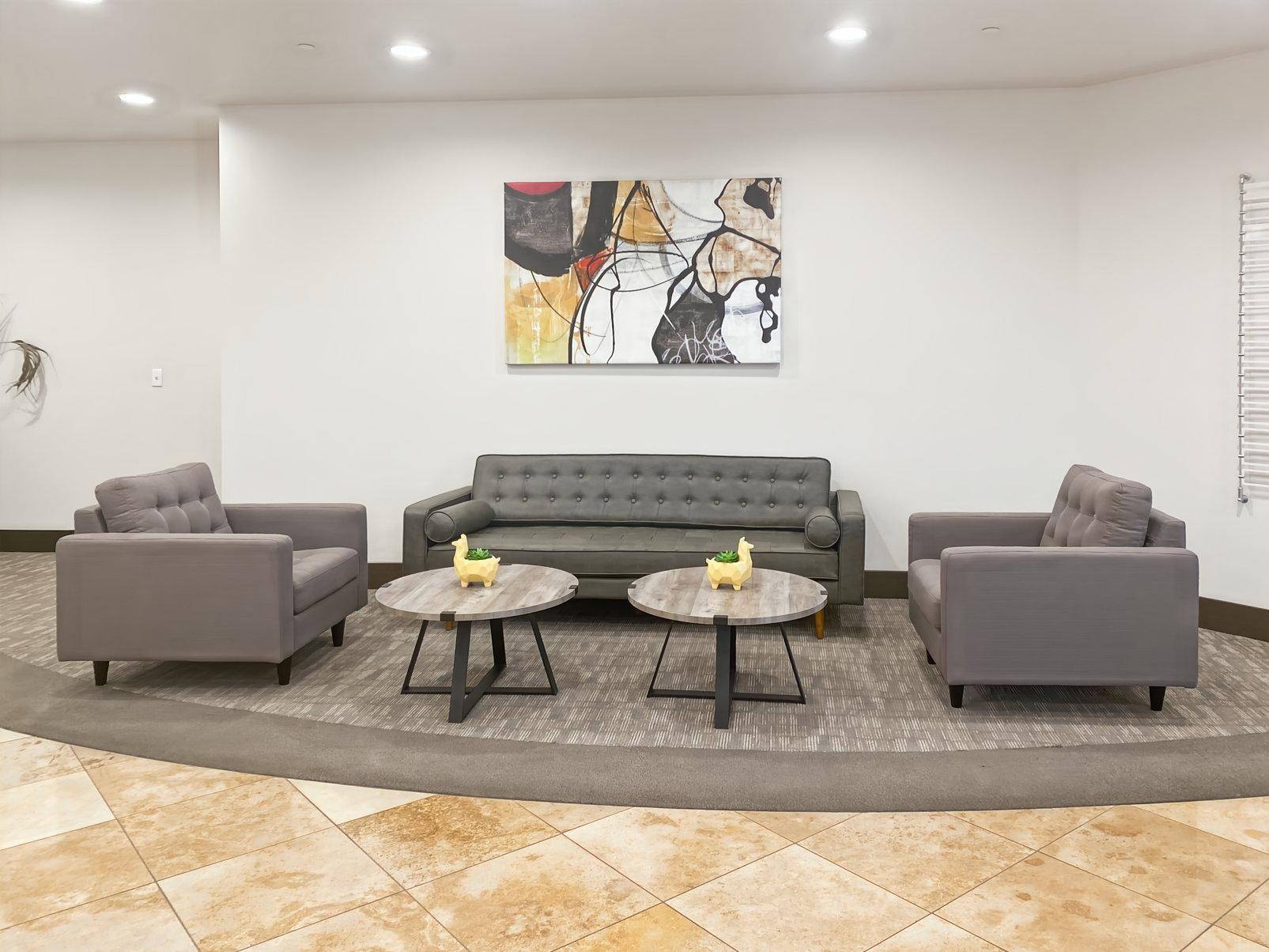 Gemütlicher Loungebereich mit grauem Sofa, Sesseln und zwei runden Couchtischen.