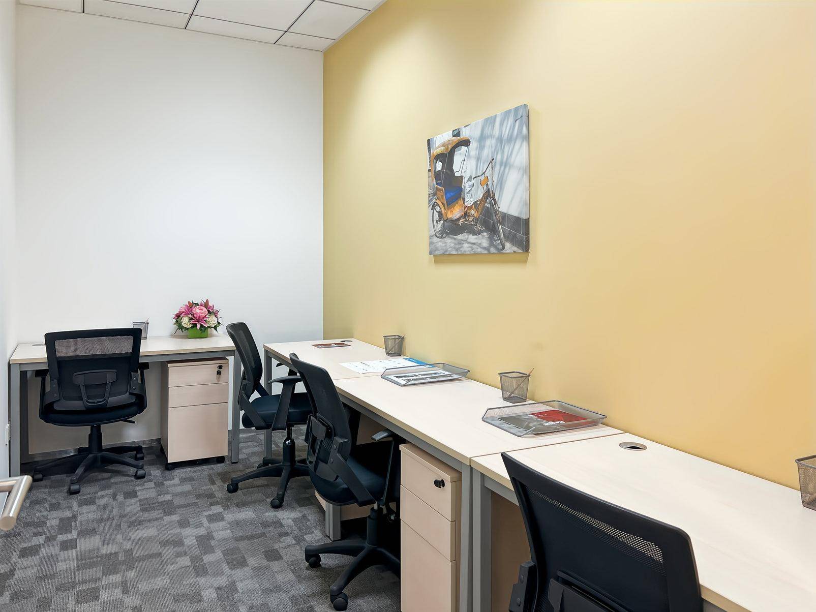 Helles Büro mit mehreren Arbeitsplätzen, gelber Akzentwand und grauem Teppichboden.