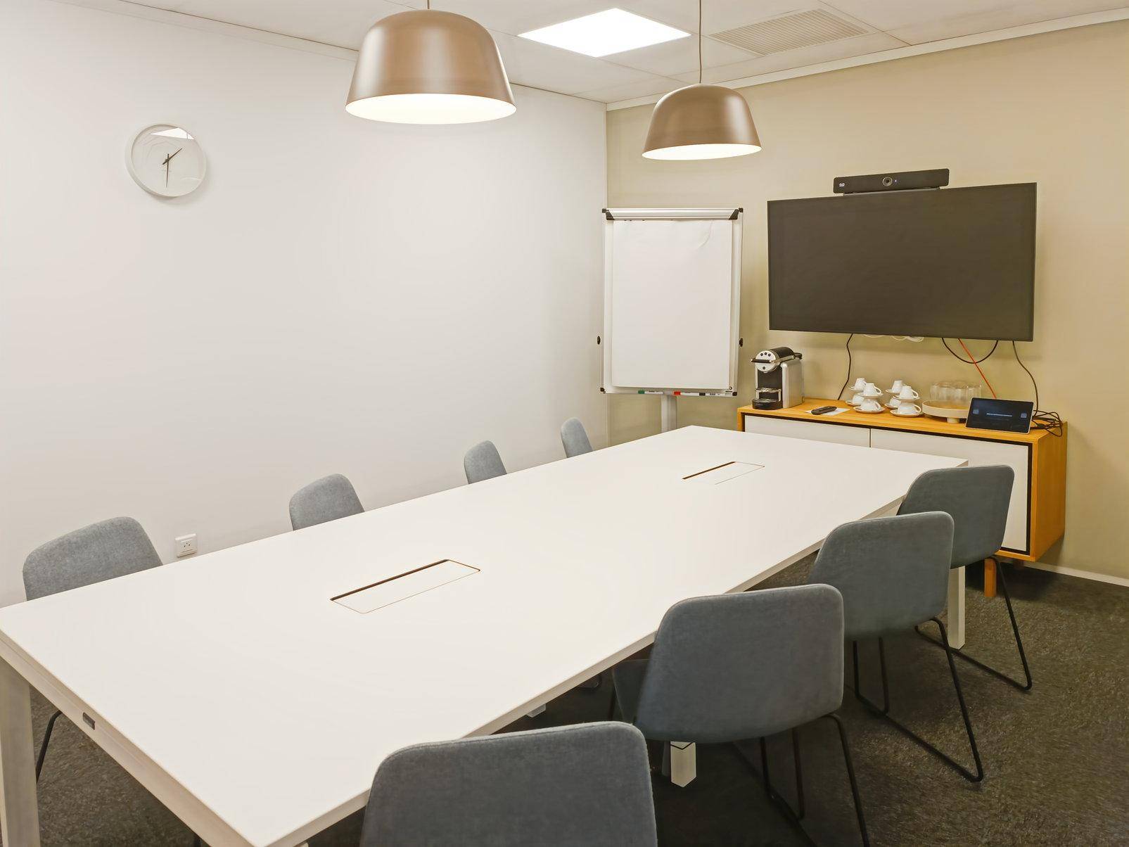 Heller Konferenzraum mit großem Tisch, bequemen Stühlen und einem Wandfernseher für Präsentationen und Meetings.