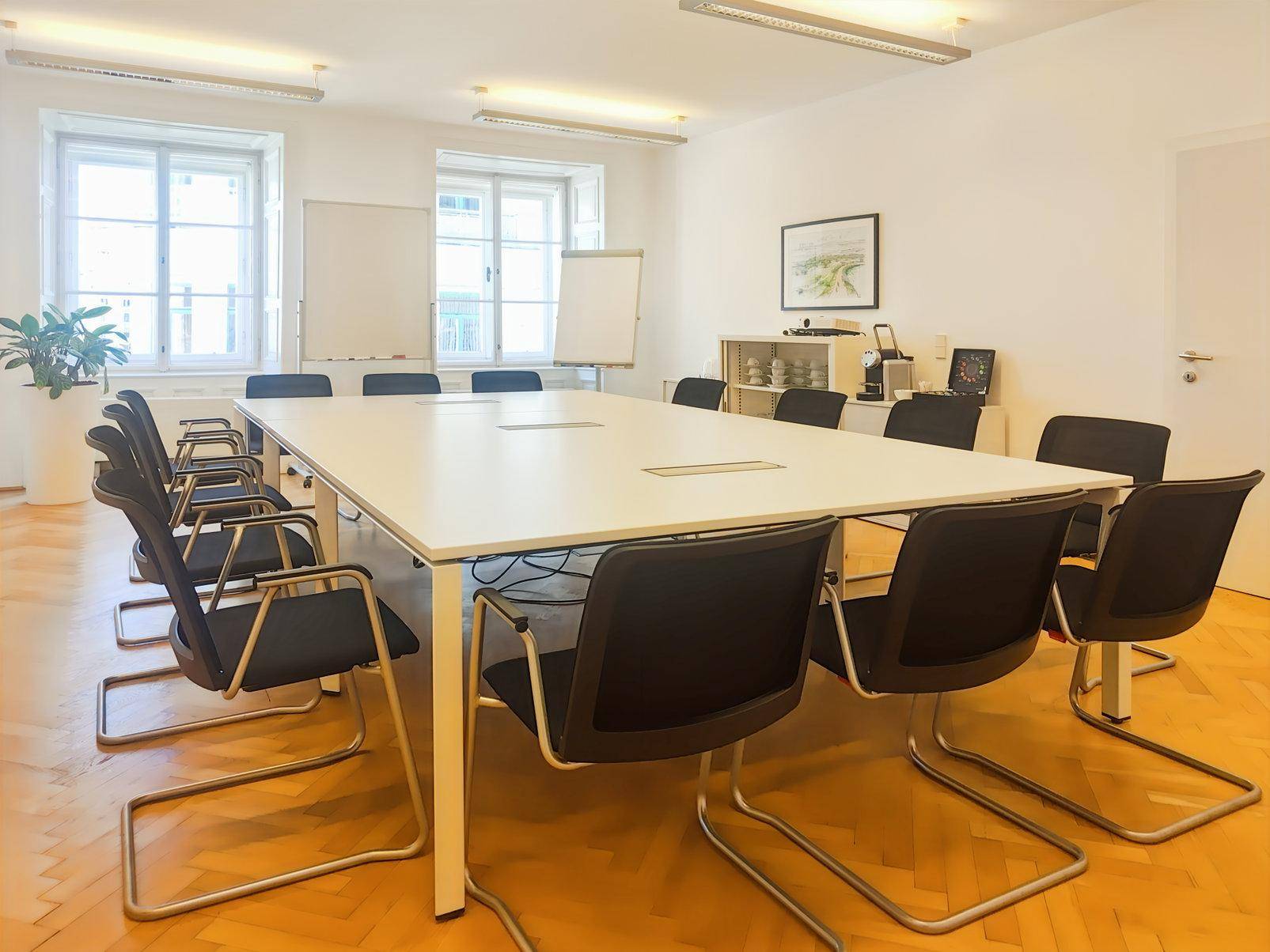 Großer Konferenzraum mit langem Tisch, vielen Stühlen und Holzparkettboden, ideal für Besprechungen.