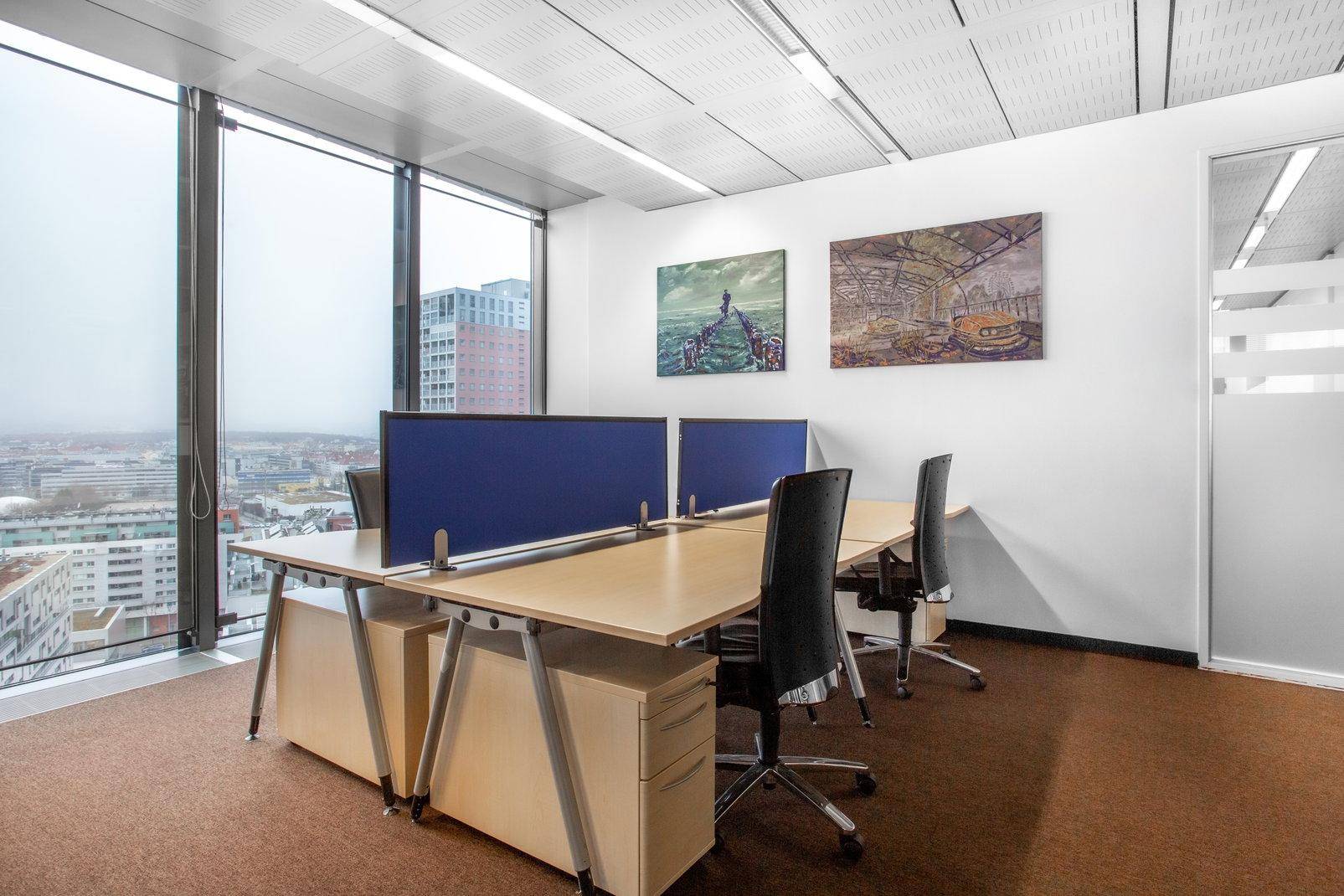Helles Büro mit zwei Arbeitsplätzen, großen Fenstern und Panoramablick auf die Stadt, modern gestaltet.