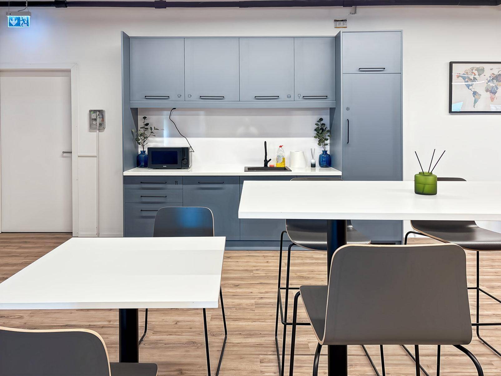 Moderne Teeküche mit blaugrauen Schränken, weißen Arbeitsplatten und Holzboden in einem Bürogebäude.