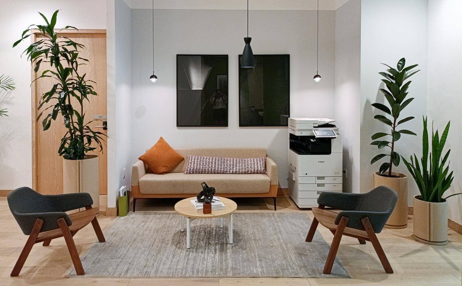 Gemütlicher Wartebereich mit beigem Sofa, zwei Sesseln, vielen Pflanzen und einem Drucker für Komfort und Funktionalität.