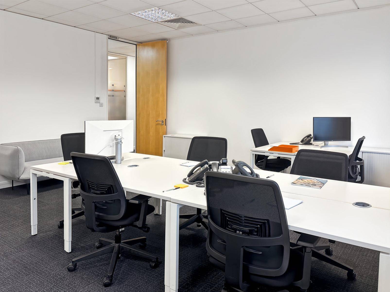 Heller Großraumbüro mit mehreren Arbeitsplätzen, modernen Schreibtischen und ergonomischen Bürostühlen.