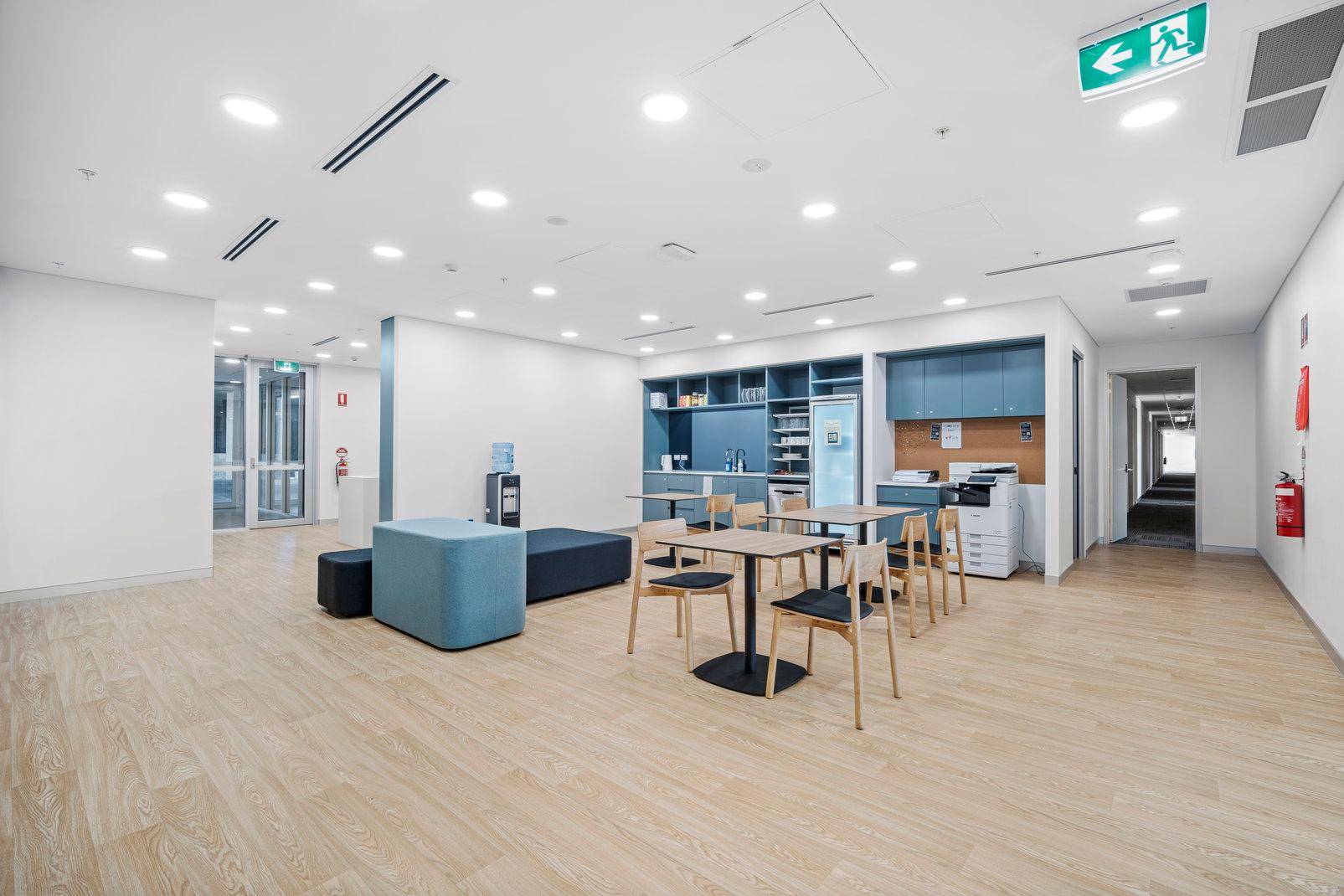 Geräumiger Pausenbereich mit einer blauen Küchenzeile, Esstischen und Sitzgelegenheiten in einem modernen Büro.