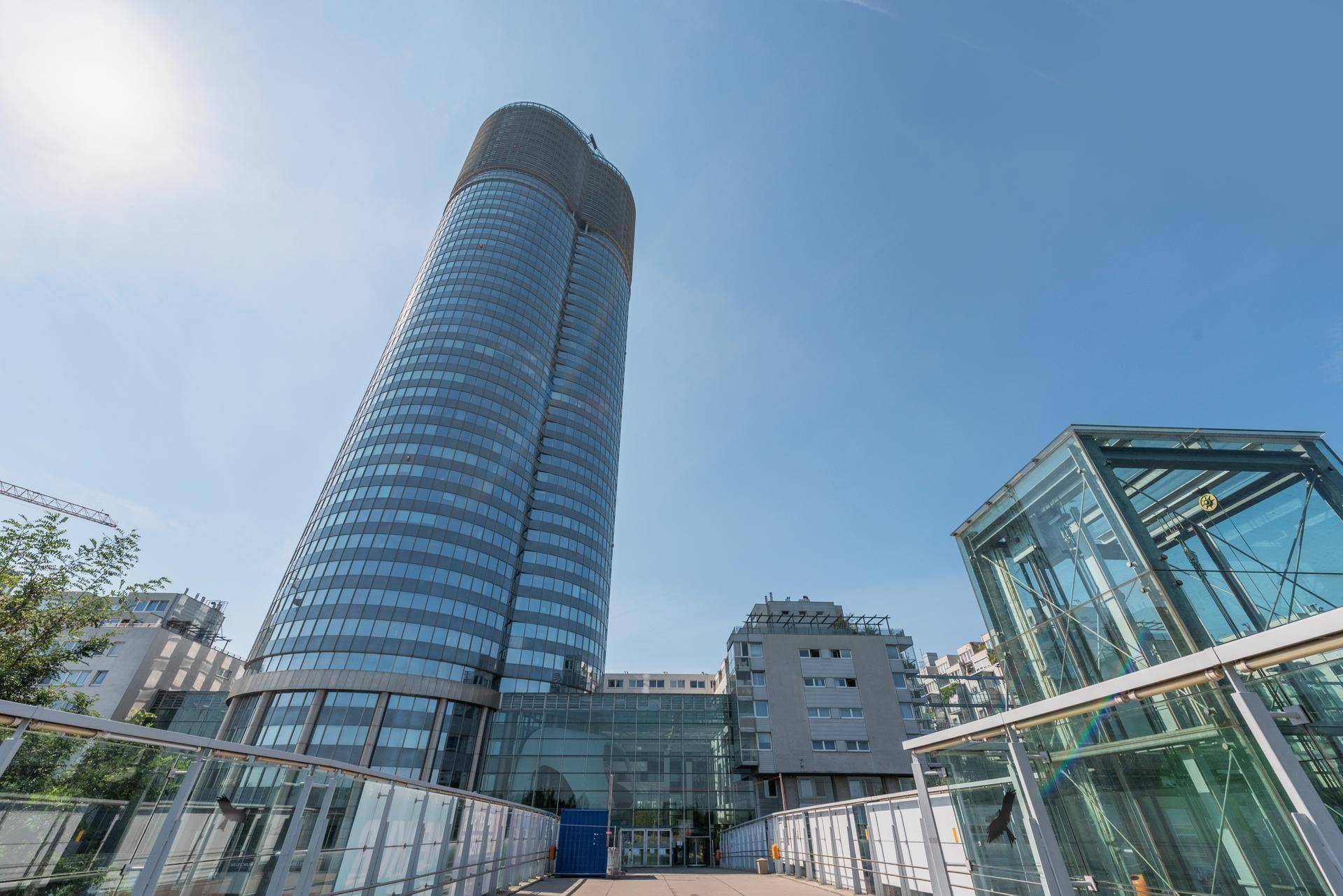 Beeindruckendes modernes Hochhaus mit Glasfassade unter strahlend blauem Himmel, umgeben von weiteren Gebäuden.