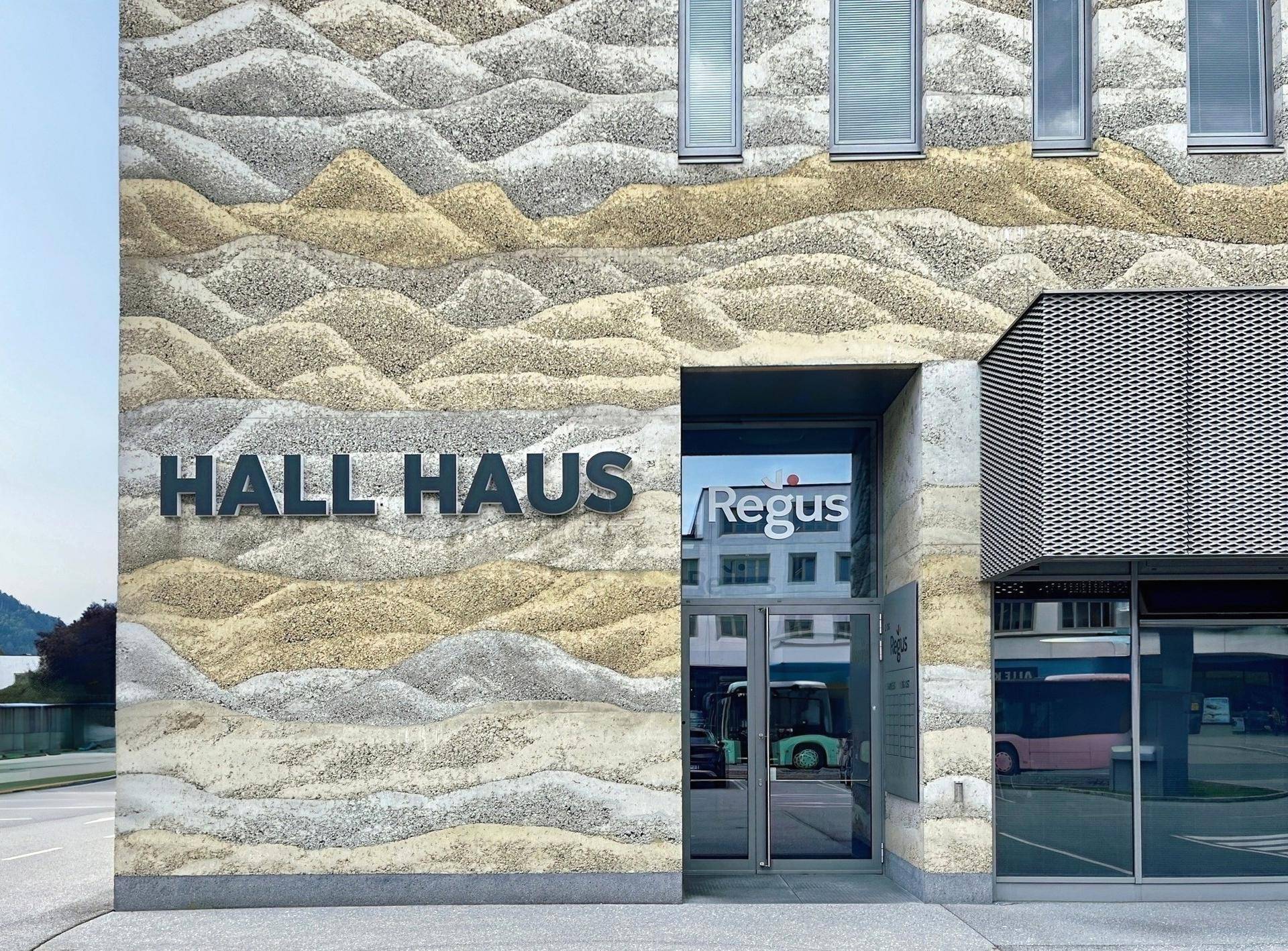Moderne Gebäudefassade mit einzigartiger wellenförmiger Textur und dem Schriftzug "HALL HAUS" über dem Eingang.