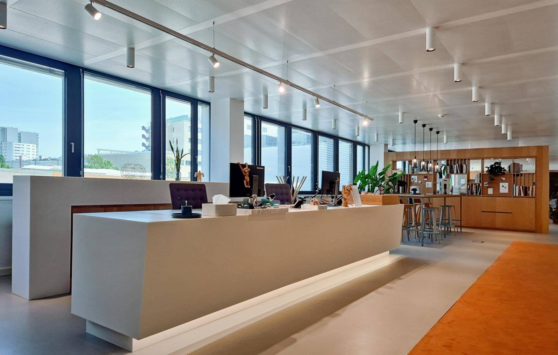 Heller, moderner Empfangsbereich in einem Büro mit großen Fenstern, minimalistischem Schreibtisch und Holzelementen.