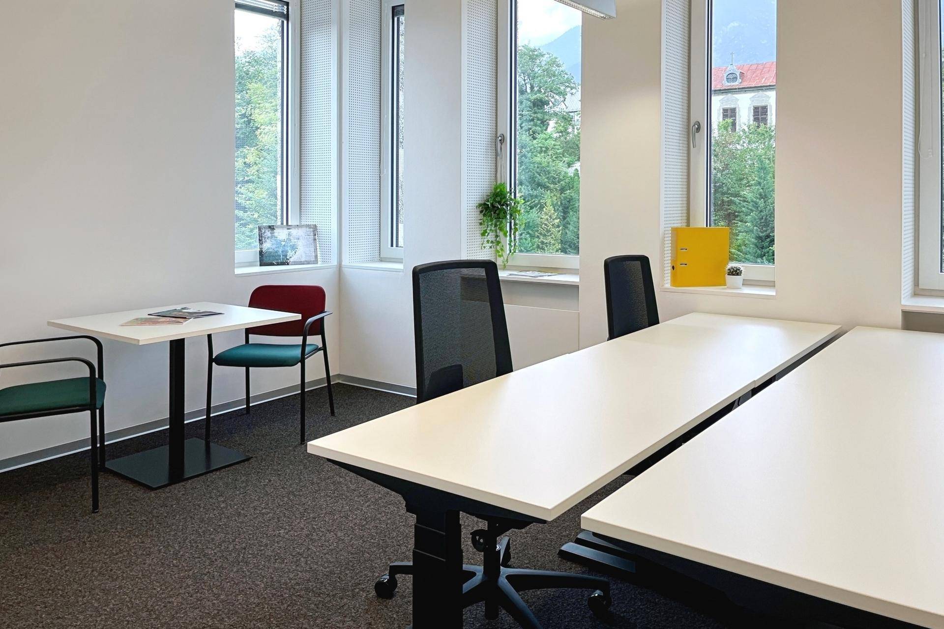 Helles Büro mit mehreren Arbeitsplätzen, großen Fenstern und Blick auf die grüne Umgebung.