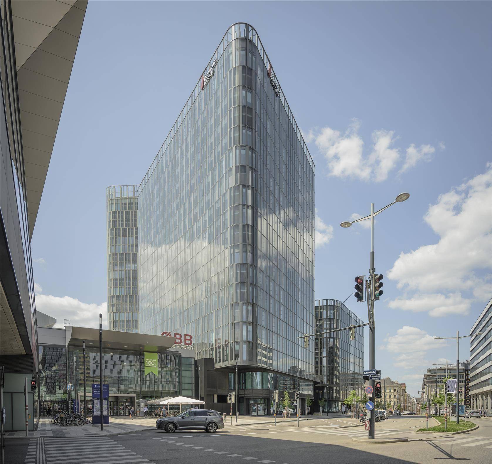 Modernes Bürogebäude mit Glasfassade an einer belebten Kreuzung unter blauem Himmel.
