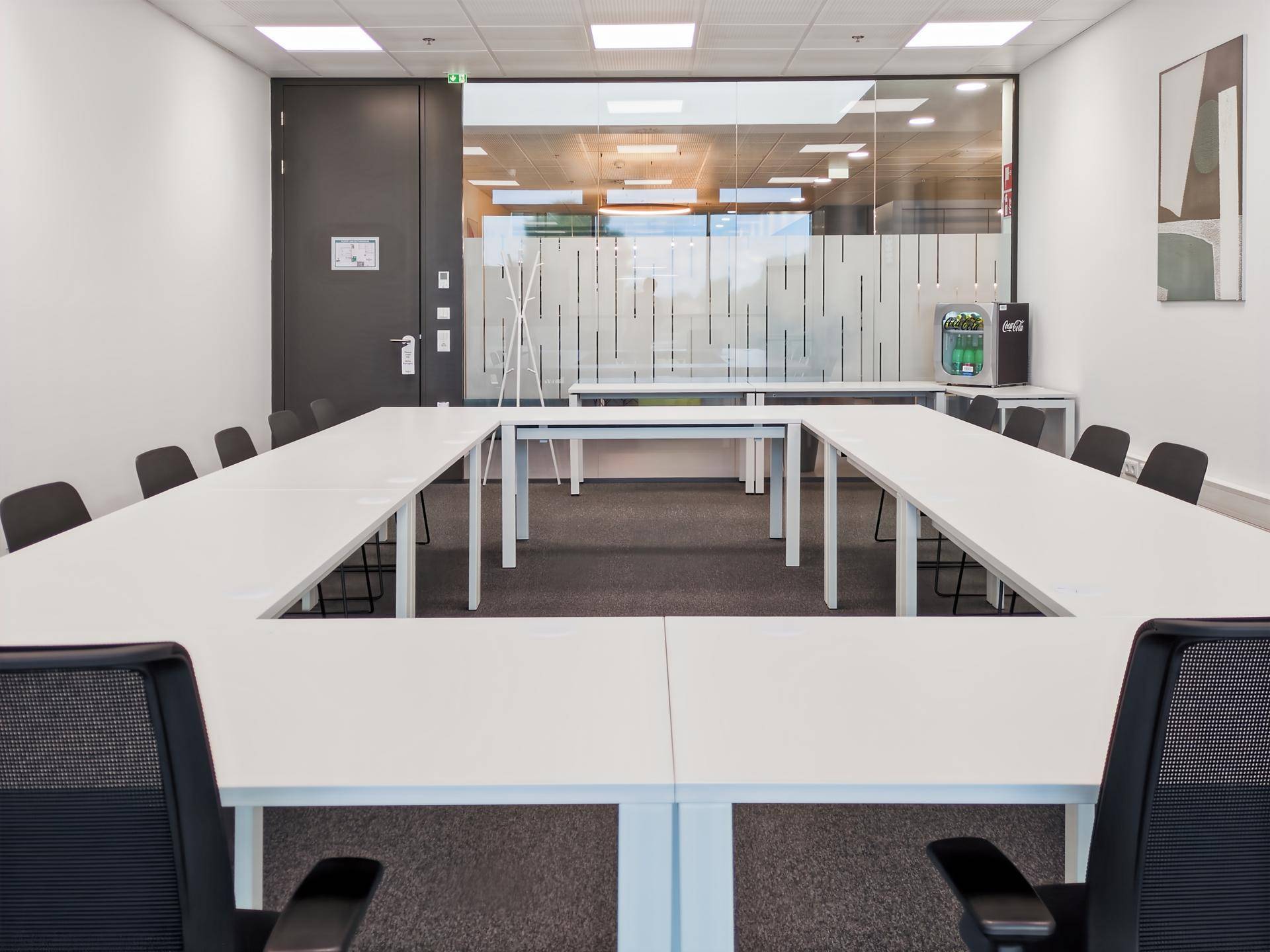 Geräumiger Konferenzraum mit U-förmiger Tischordnung, ergonomischen Stühlen und einer Glaswand zum Flur.