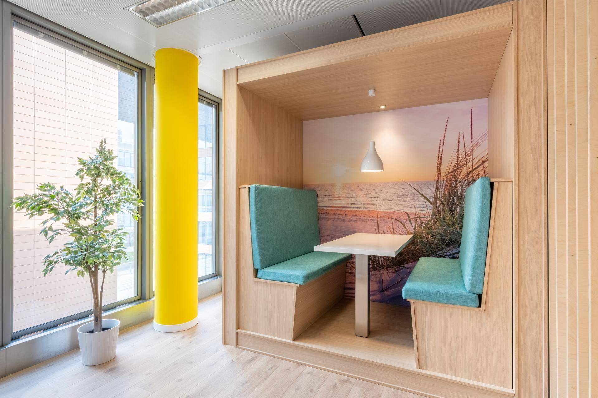 Gemütliche Arbeitskabine in einem Büro mit Holzelementen, blauen Sitzpolstern und einer Strandtapete.
