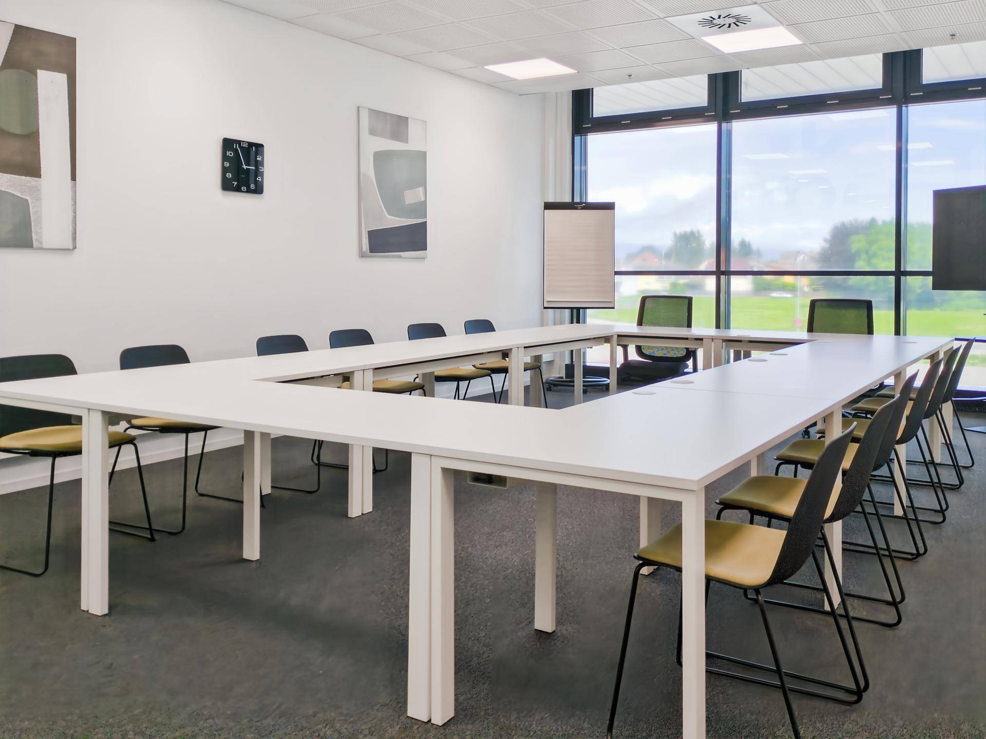 Großer Konferenzraum mit U-förmigem Tisch, vielen Stühlen und großen Fenstern mit Blick ins Grüne.