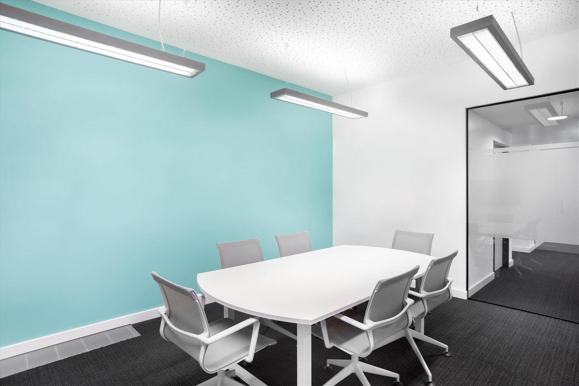 Moderner Besprechungsraum mit weißem Tisch, grauen Stühlen und einer farbigen Akzentwand, ideal für kreative Meetings.